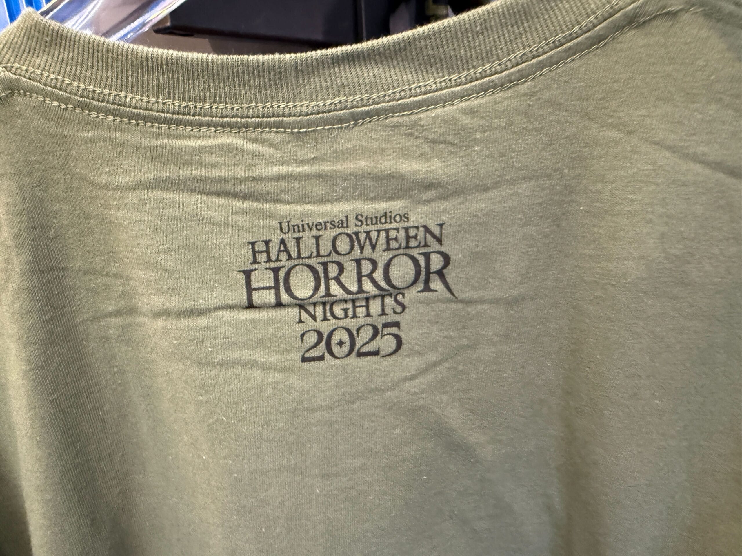 A green shirt featuring "Universal Studios Halloween Horror Nights 2025" and exclusive Lil Boo Merchandise.