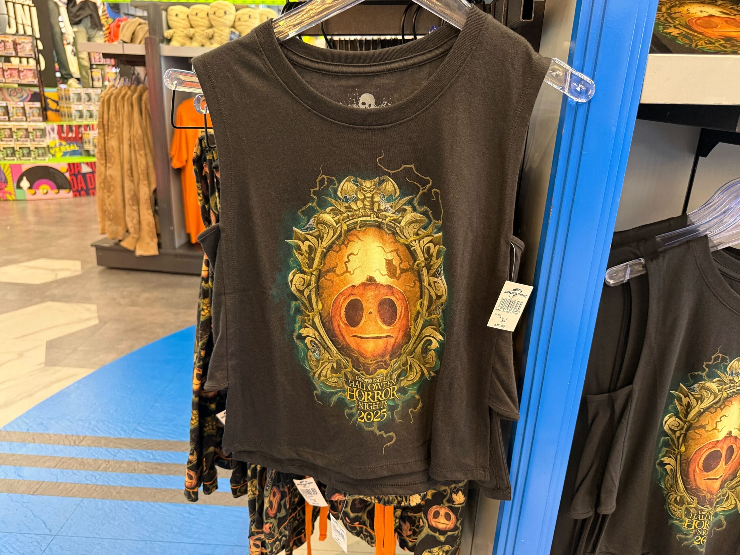 Black sleeveless shirt with a spooky golden pumpkin face, "Halloween Horror Nights 2023," and Lil Boo Merchandise displayed in-store.