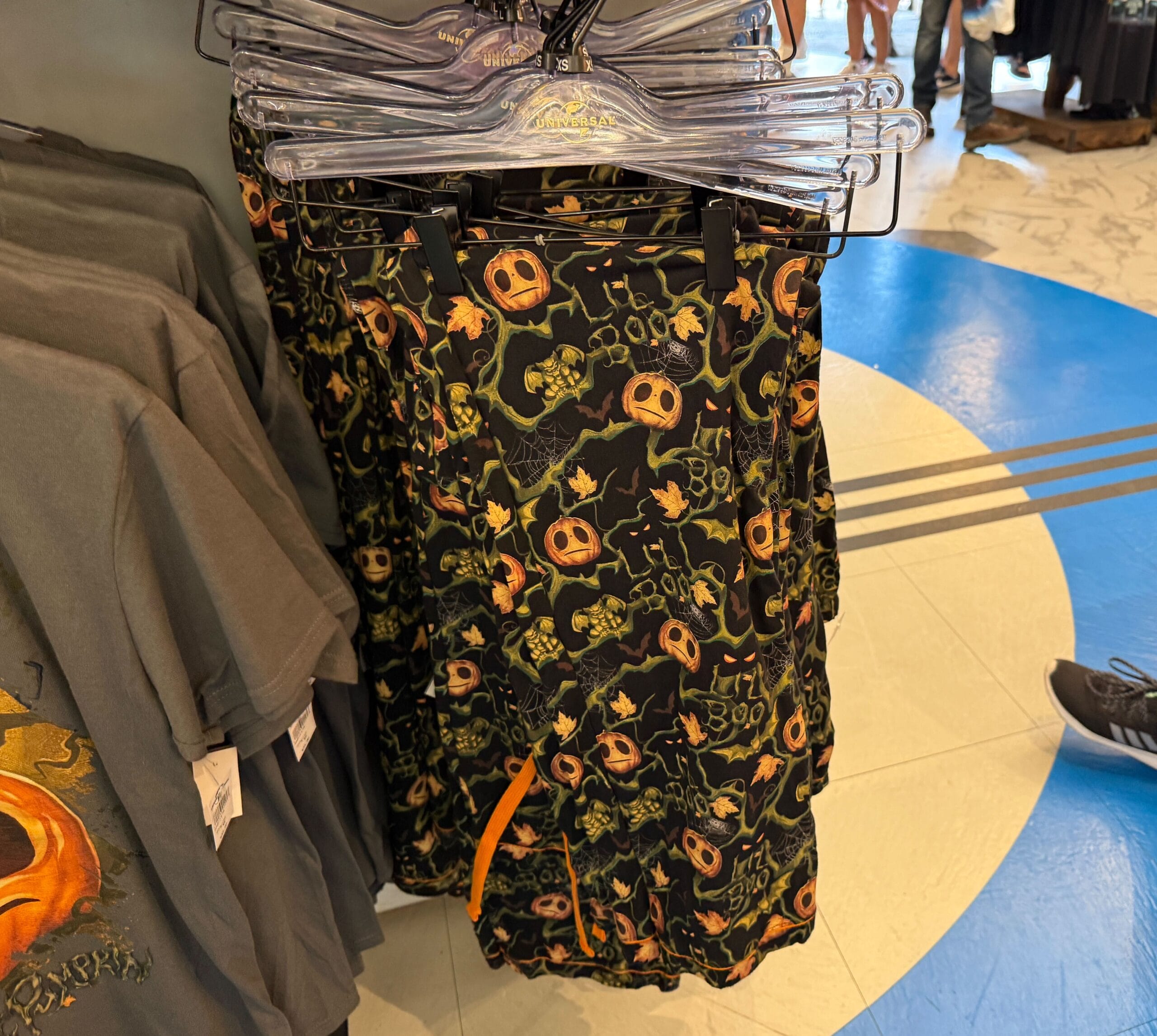 Black shorts with orange Halloween-themed Lil Boo Merchandise designs, like pumpkins, skulls, and “BOO!”, on a rack.