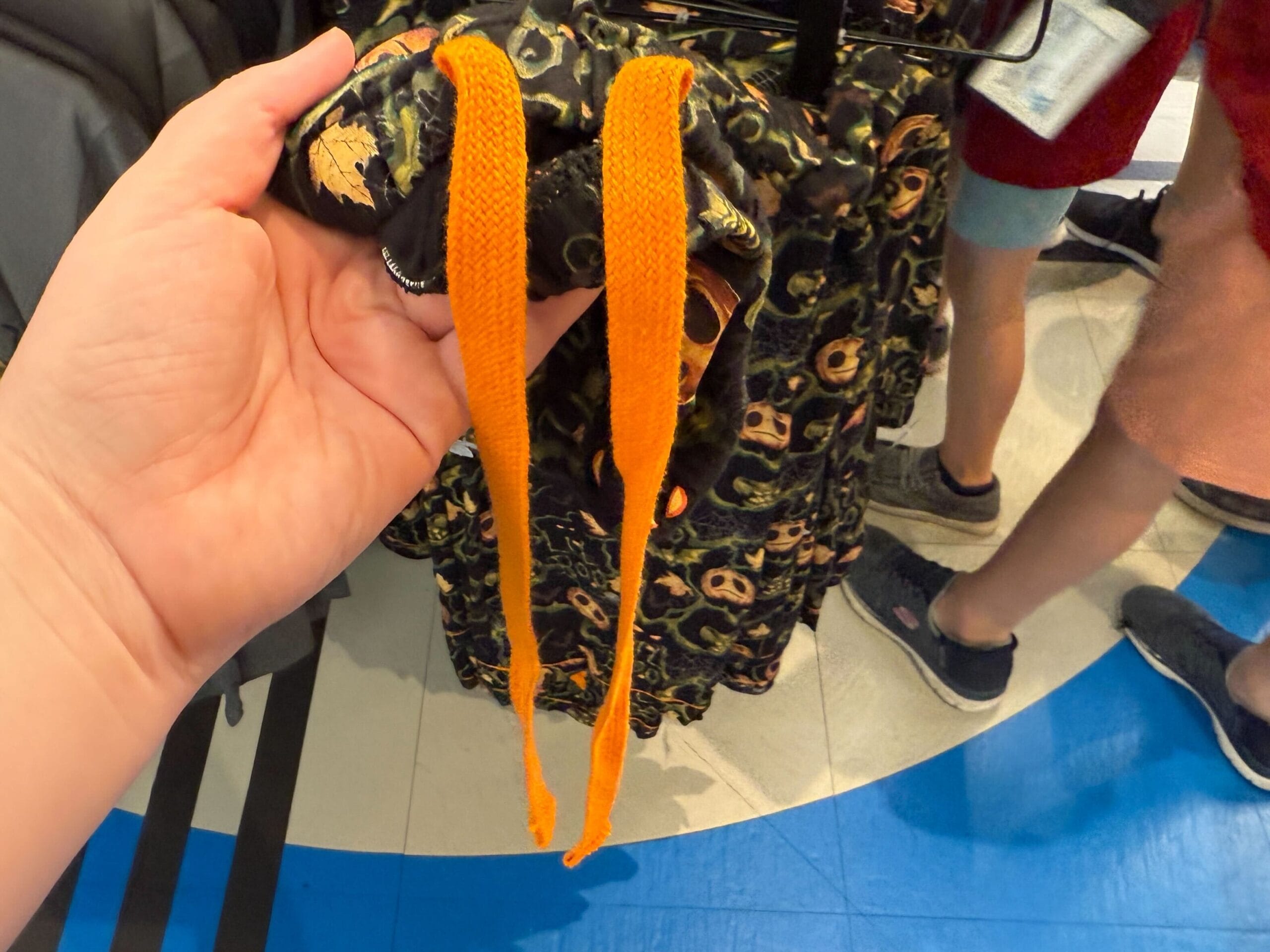 A hand holds Lil Boo Merchandise—a garment with black and yellow patterns and long orange drawstrings in a store.
