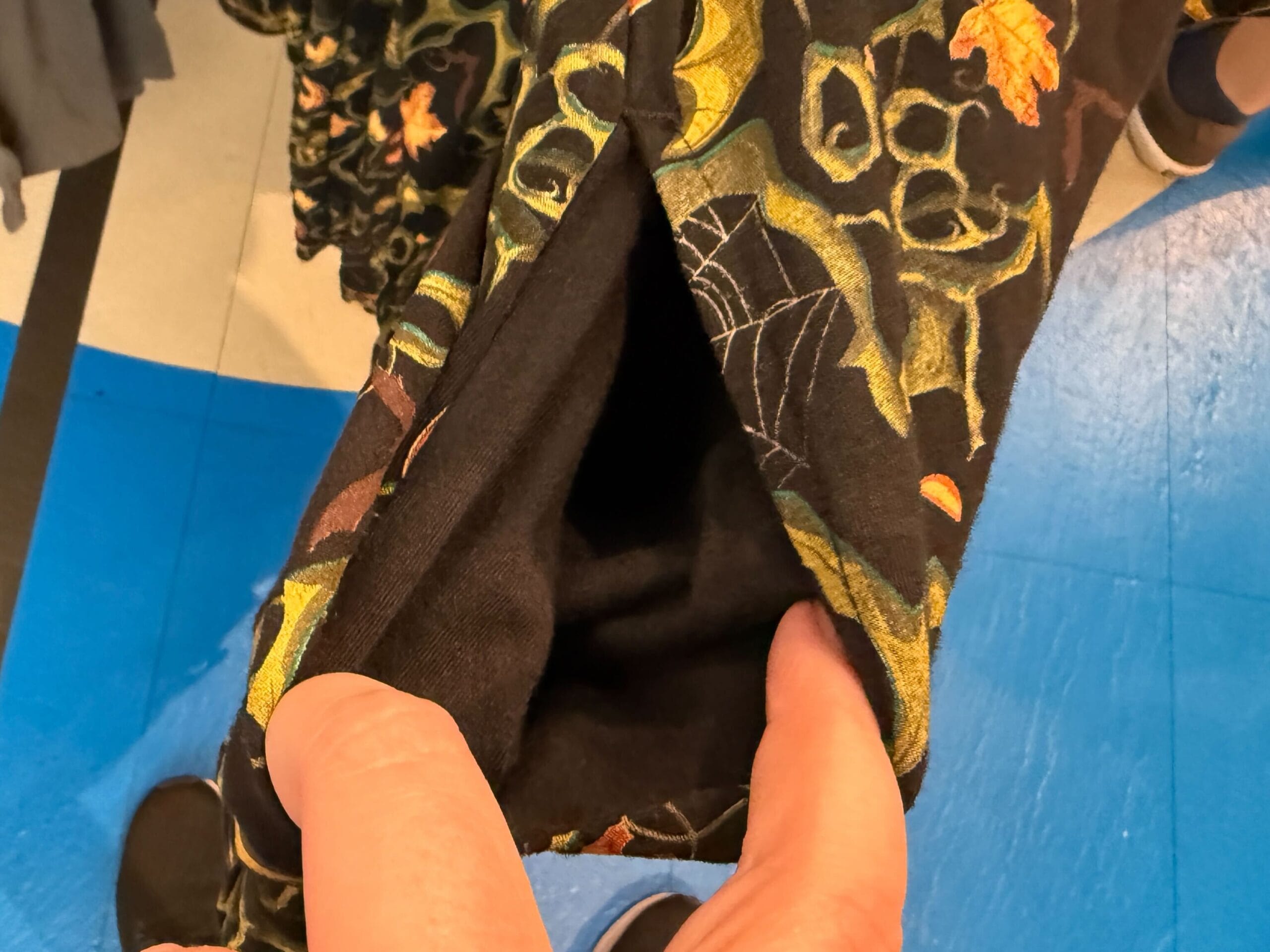 A hand holds open a black pocket on Lil Boo Merchandise fabric with a green and orange botanical pattern.
