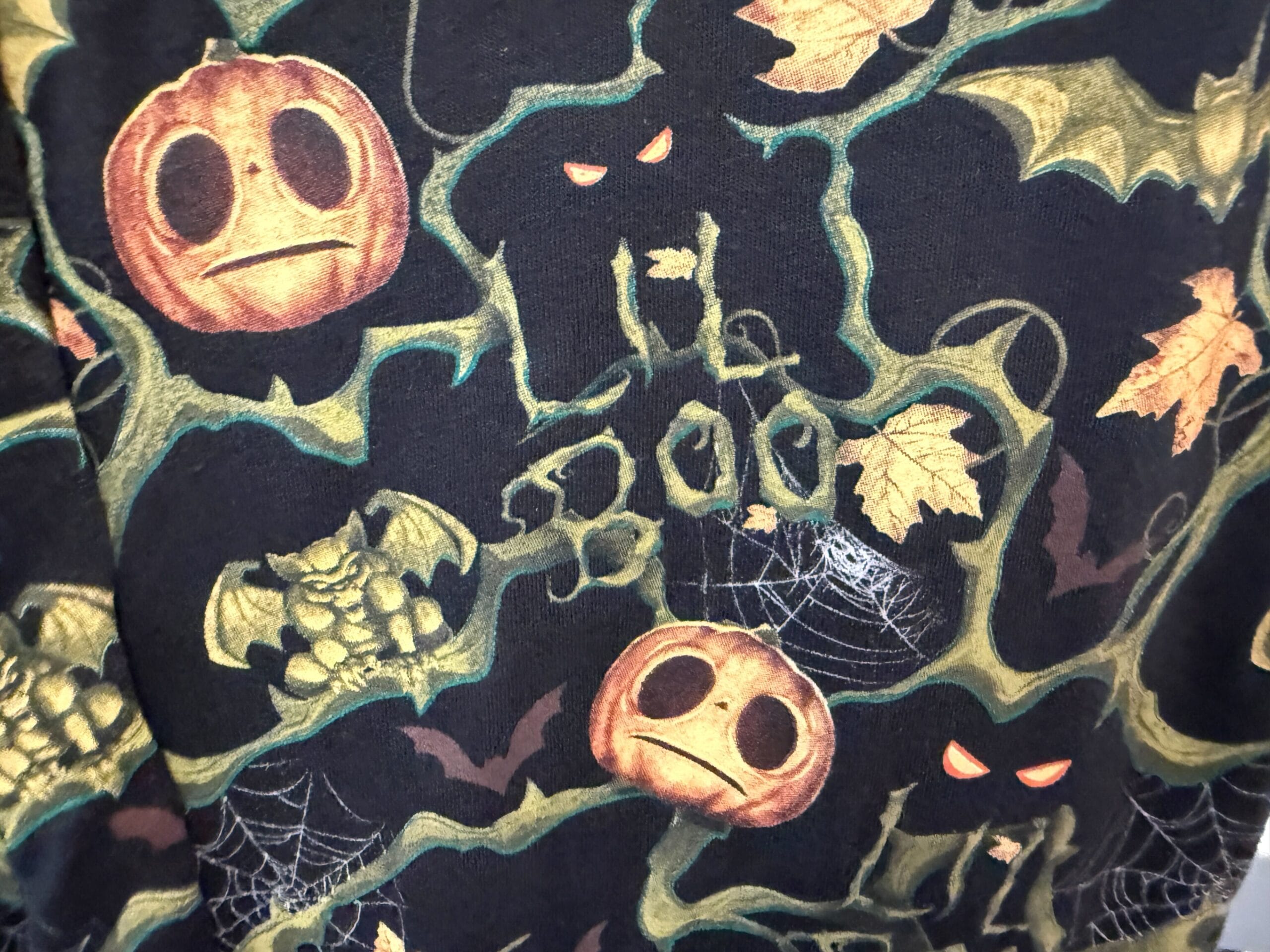 Halloween-themed Lil Boo Merchandise fabric with jack-o'-lanterns, bats, leaves, and spooky faces on a black background.