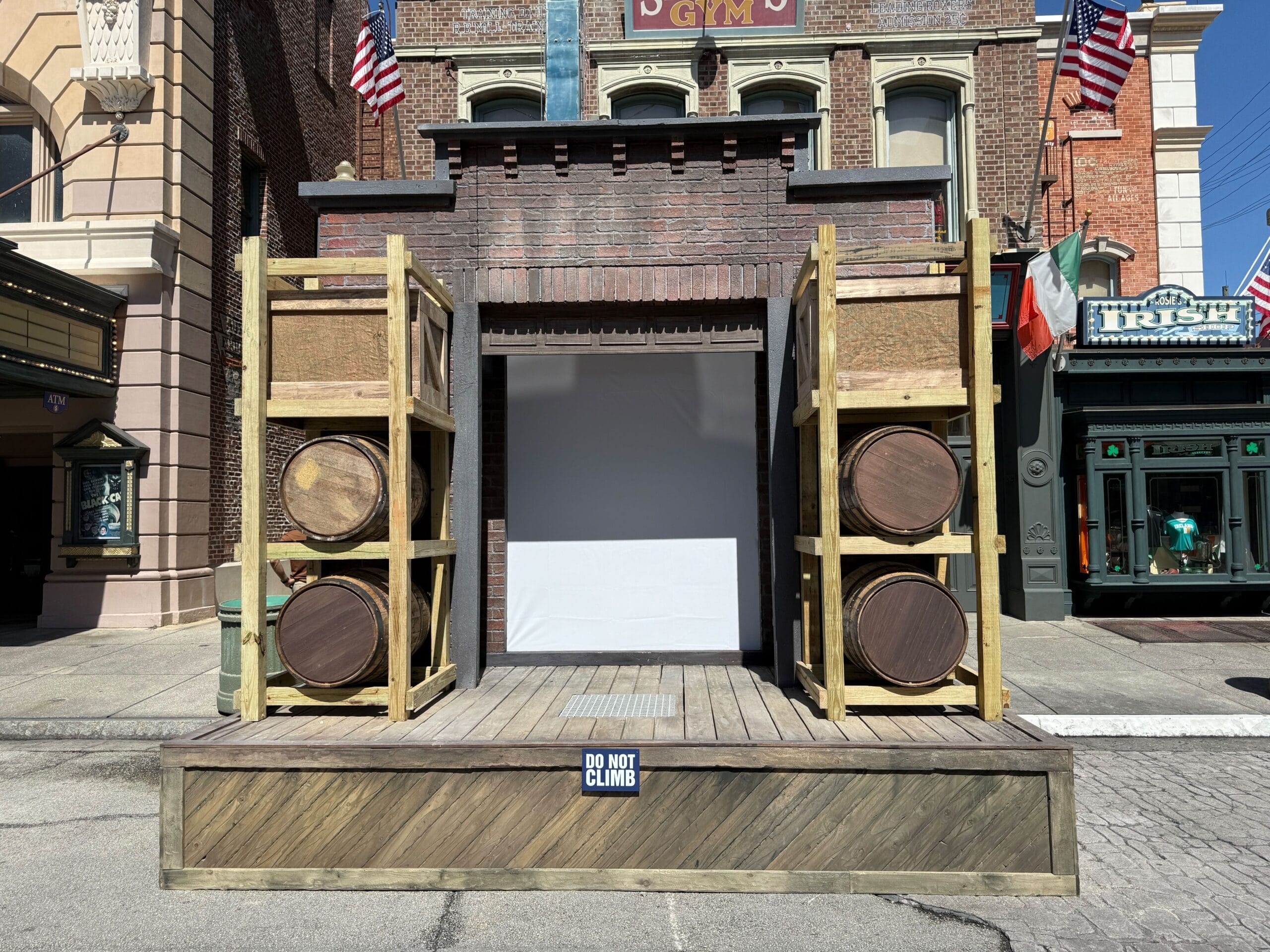 Small wooden stage with barrels on each side, a brick backdrop, and a "Do Not Climb" sign in front.