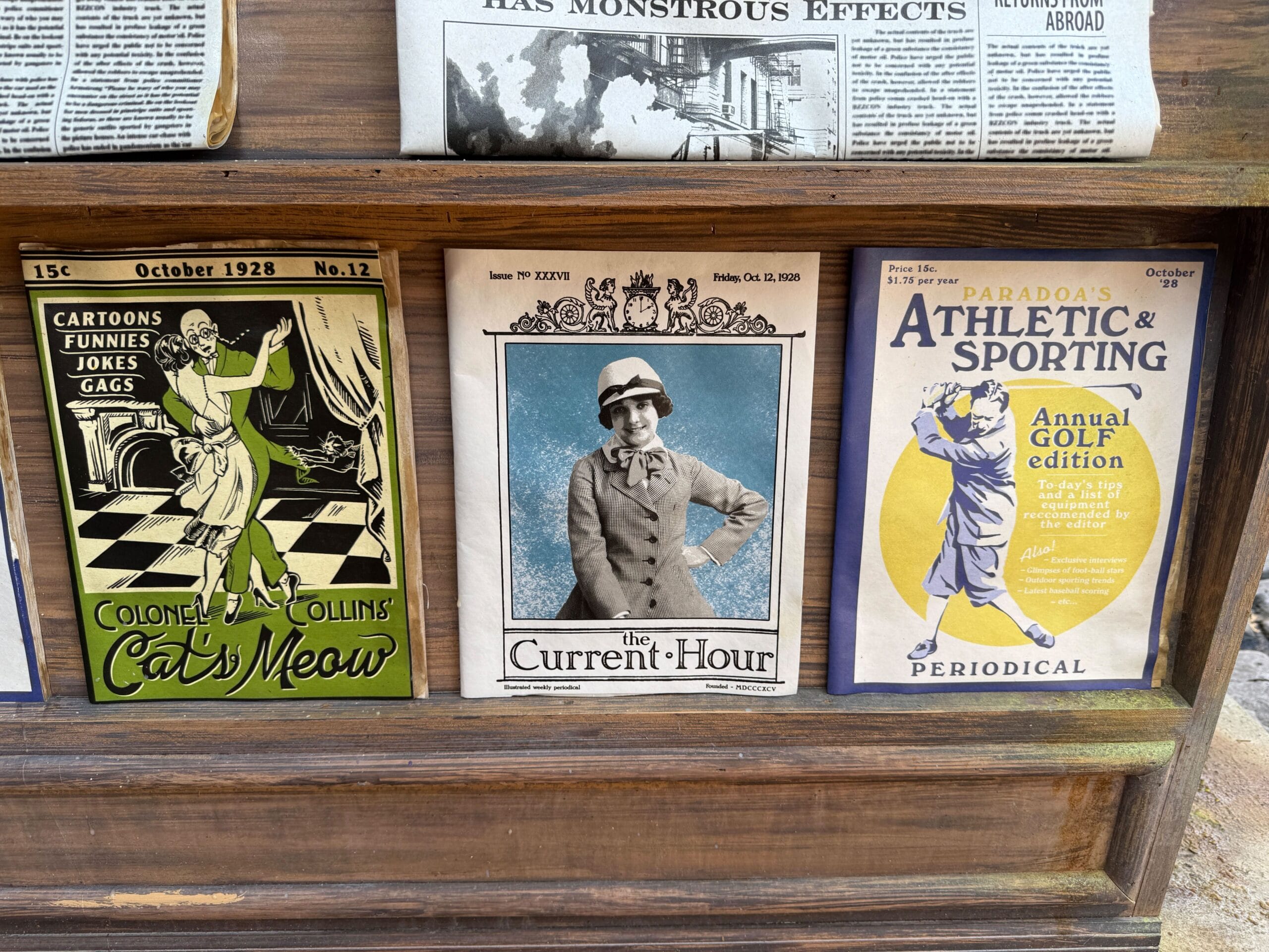 Three vintage magazine covers displayed side by side in a wooden rack, each with illustrated or black-and-white covers.