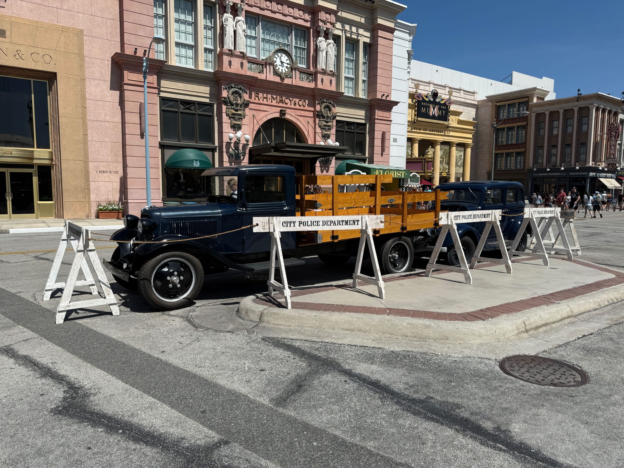 Vintage police truck behind wooden barriers labeled "City Police Department" on a sunny city street.