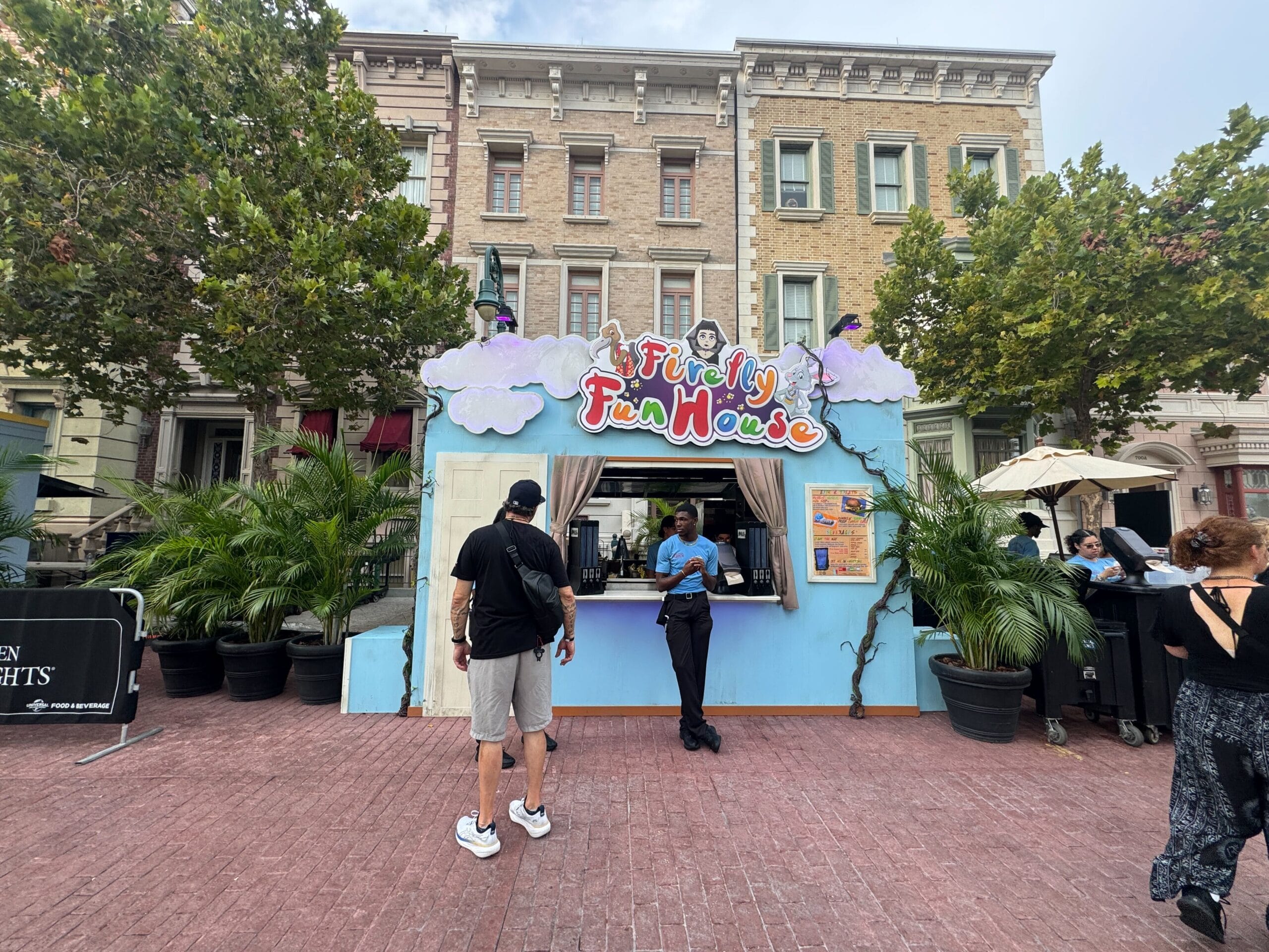 A colorful “Fiendfy Fun House” booth with people standing outside, set against tall buildings and trees.