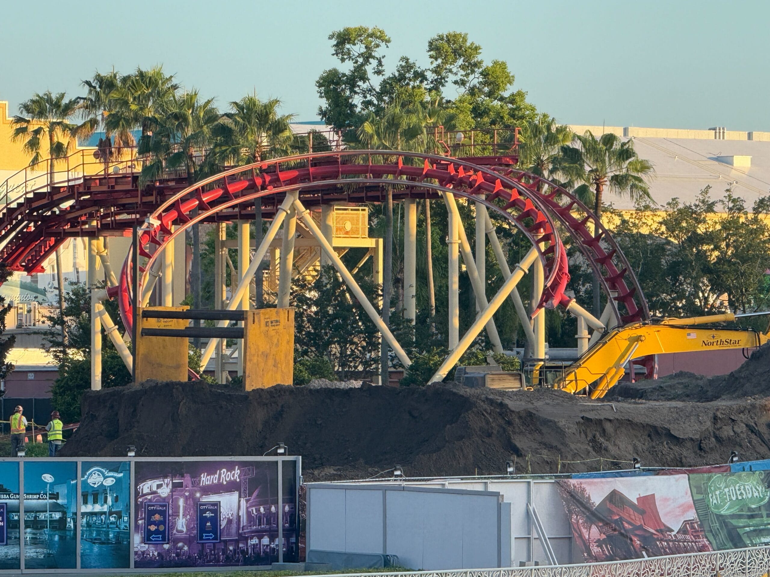 A red roller coaster, Hollywood Rip Ride Rockit at Universal Studios, loops above demolition crews and palm trees.