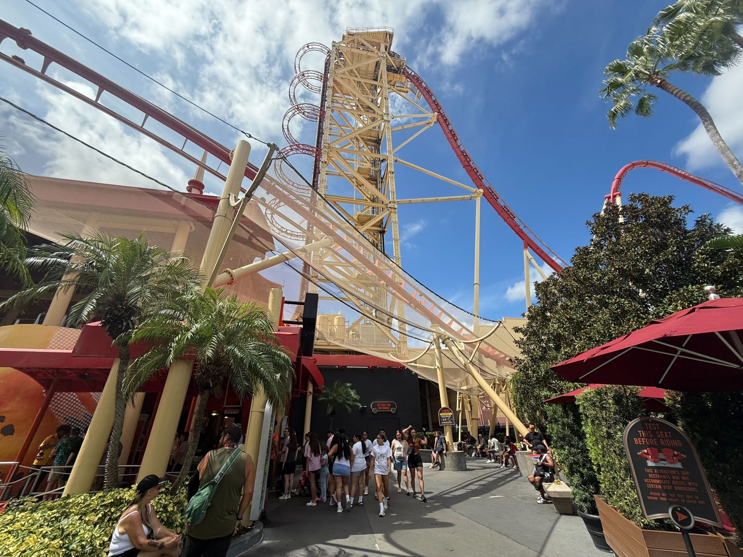 People queue outside the tall Hollywood Rip Ride Rockit coaster at Universal Studios Florida under a partly cloudy sky.