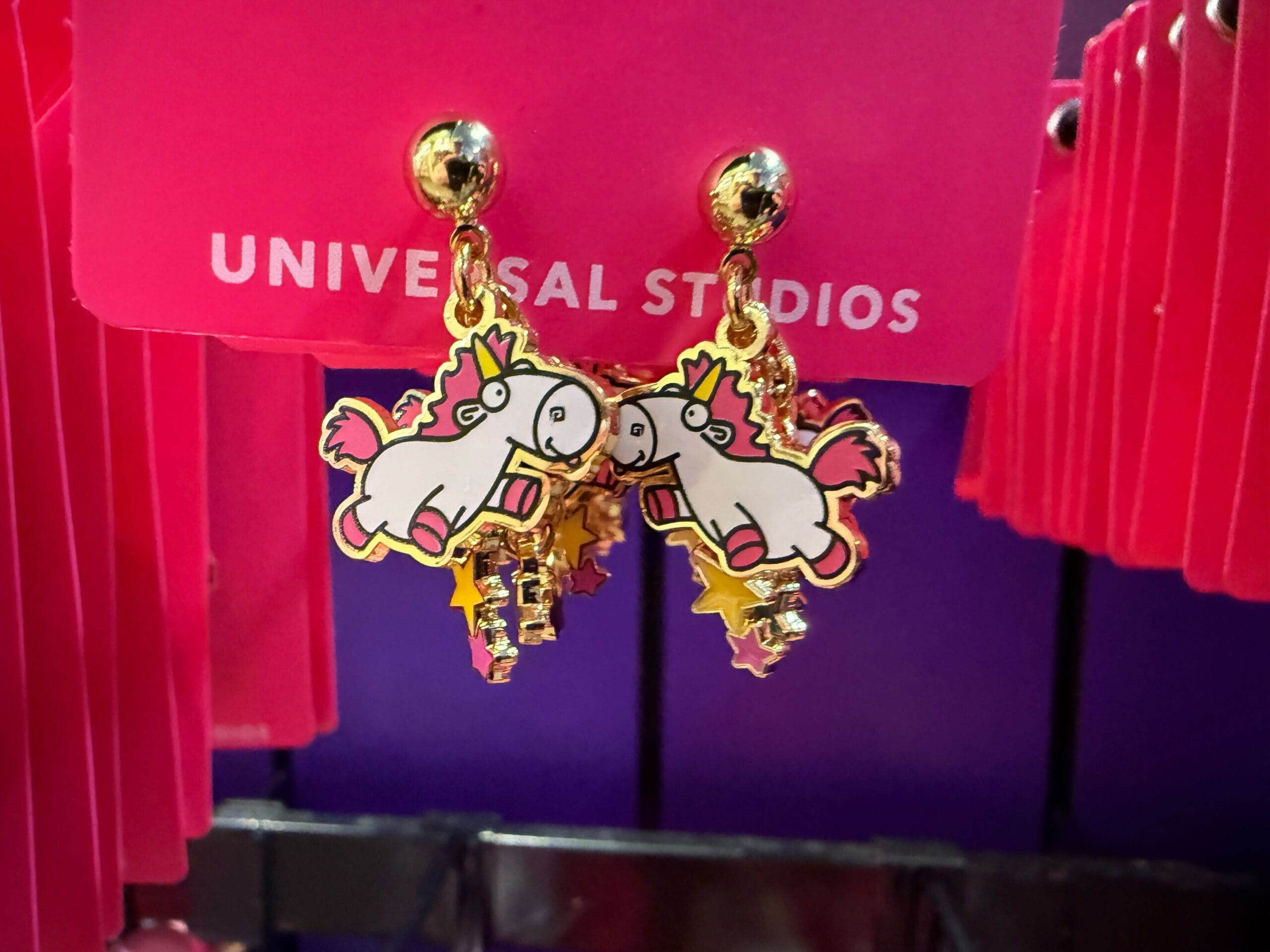 Gold unicorn earrings with pink and yellow accents on a Universal Orlando Resort display card.