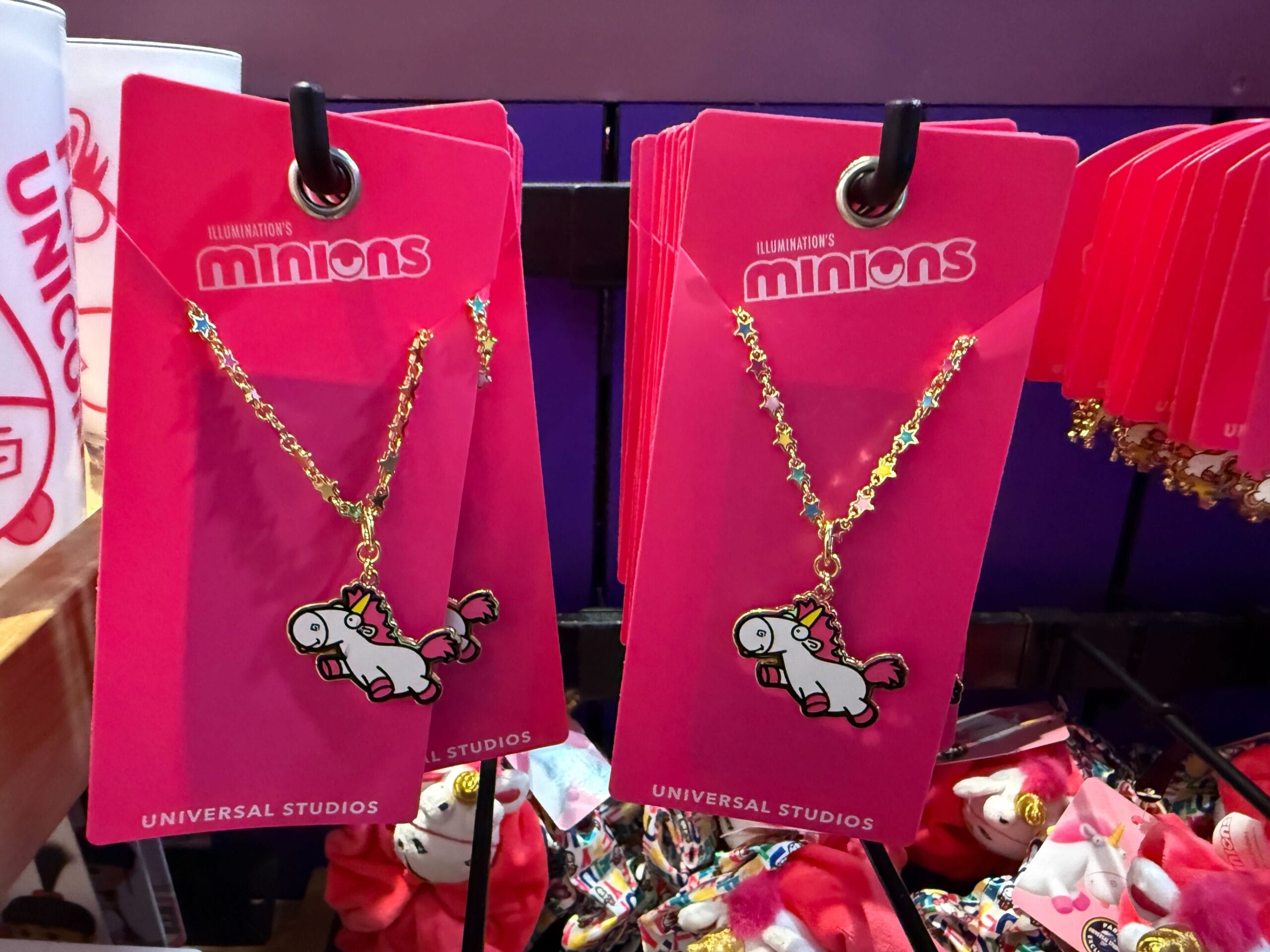 Two Fluffy Unicorn necklaces on pink Minions-themed cards, displayed for sale at Universal Orlando Resort.