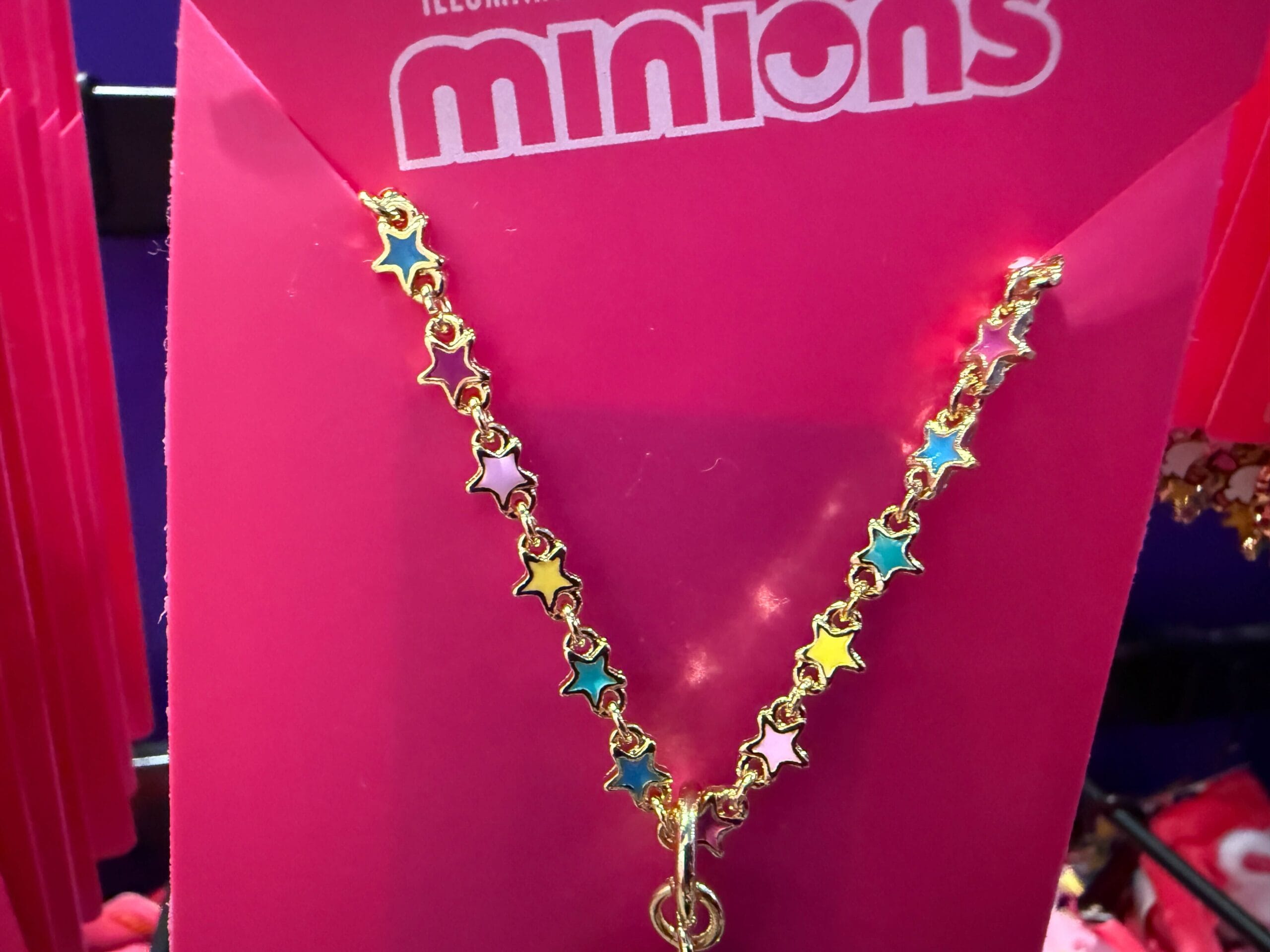 A gold chain necklace with colorful star charms on bright pink Fluffy Unicorn Minions-themed packaging.