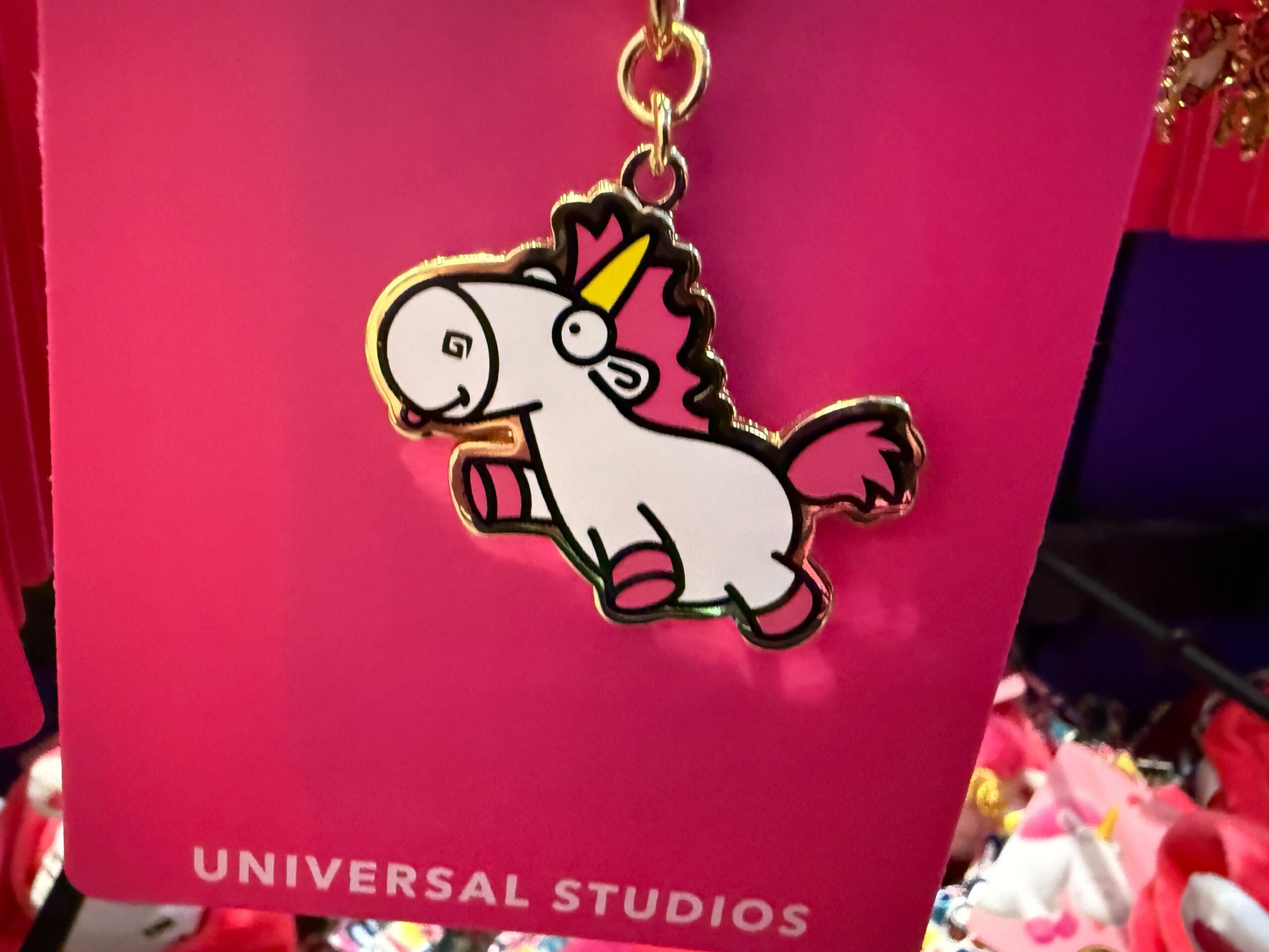 A keychain of a cute Fluffy Unicorn with a pink mane, on a bright pink Universal Orlando Resort card.