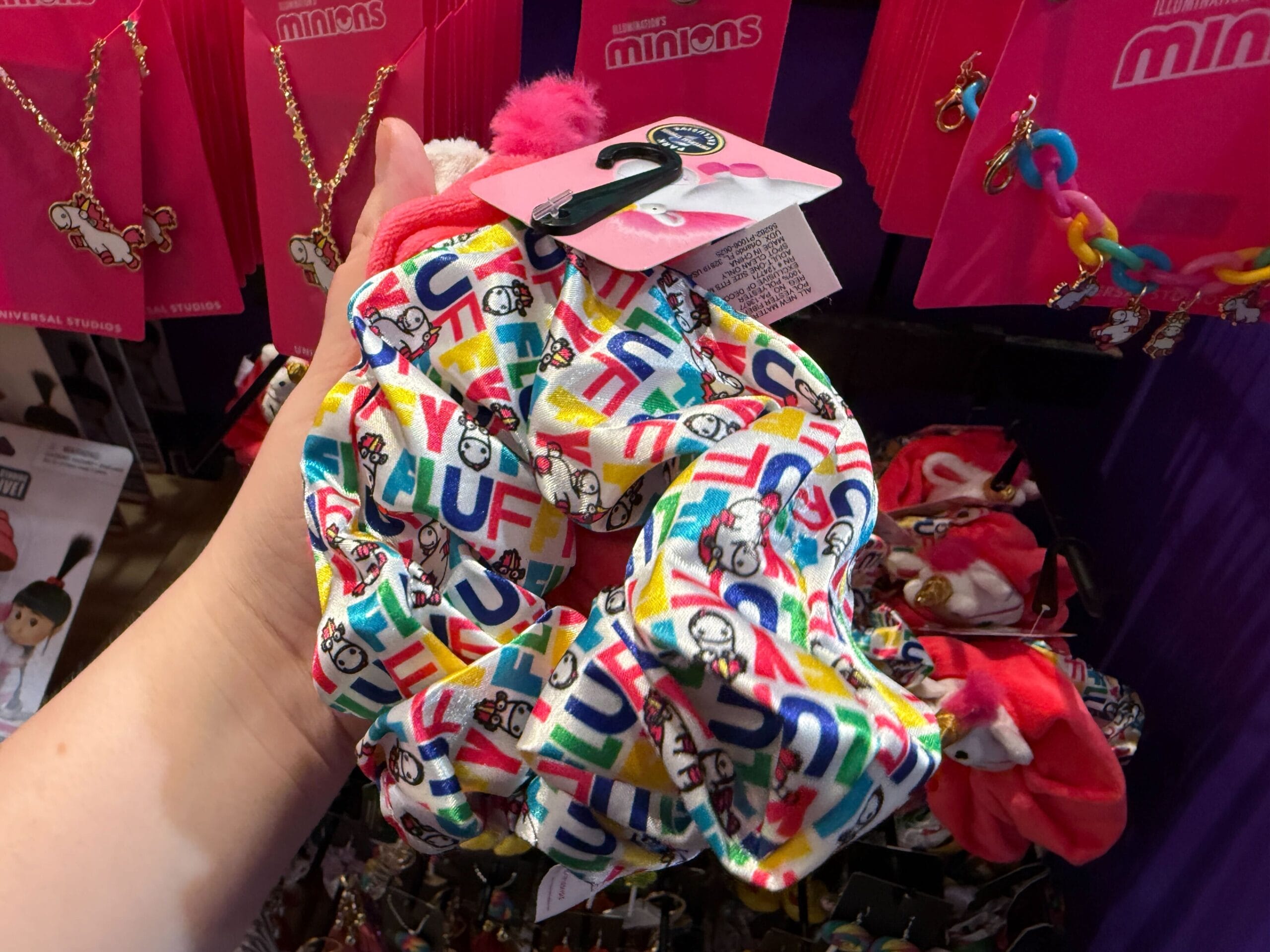 A hand holds colorful Minions scrunchies, displayed in a store with Universal Orlando Resort merchandise in the background.