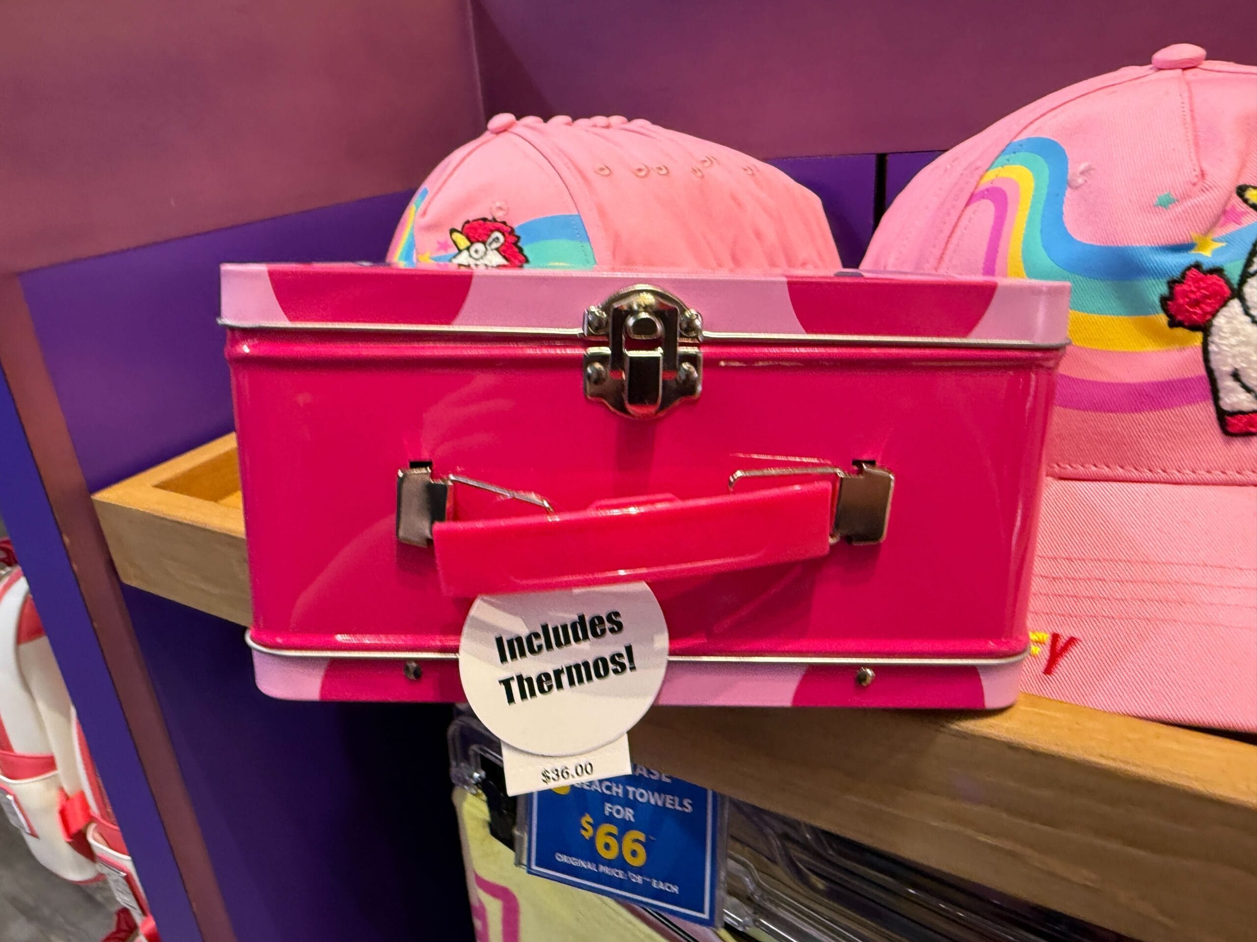 A pink lunchbox with "Includes Thermos!" stands near pink Fluffy Unicorn hats at Universal Orlando Resort.