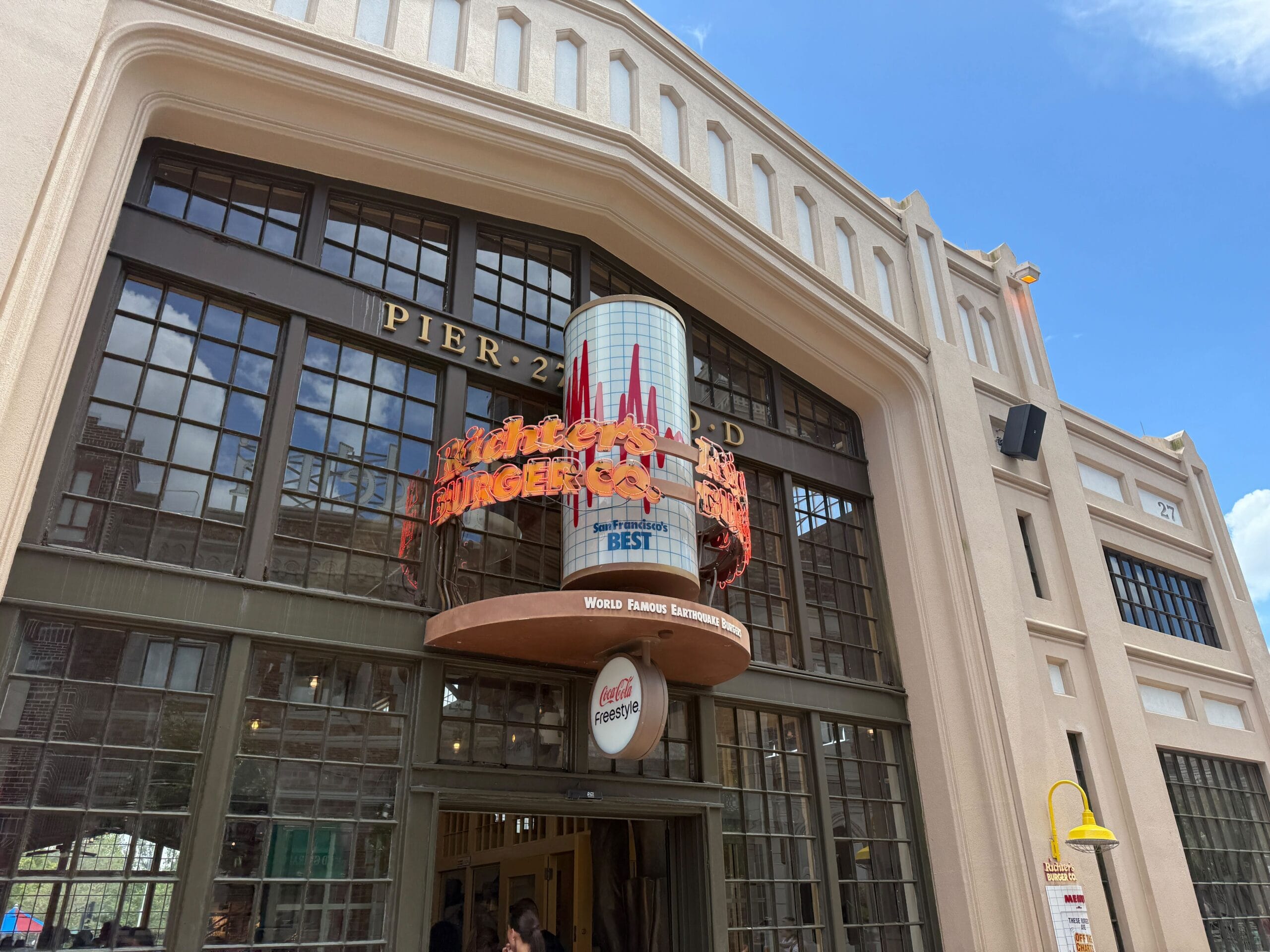 Entrance of a building with a sign reading "Pier 21" and "Richter’s Burger Co" above large glass doors on a sunny day.