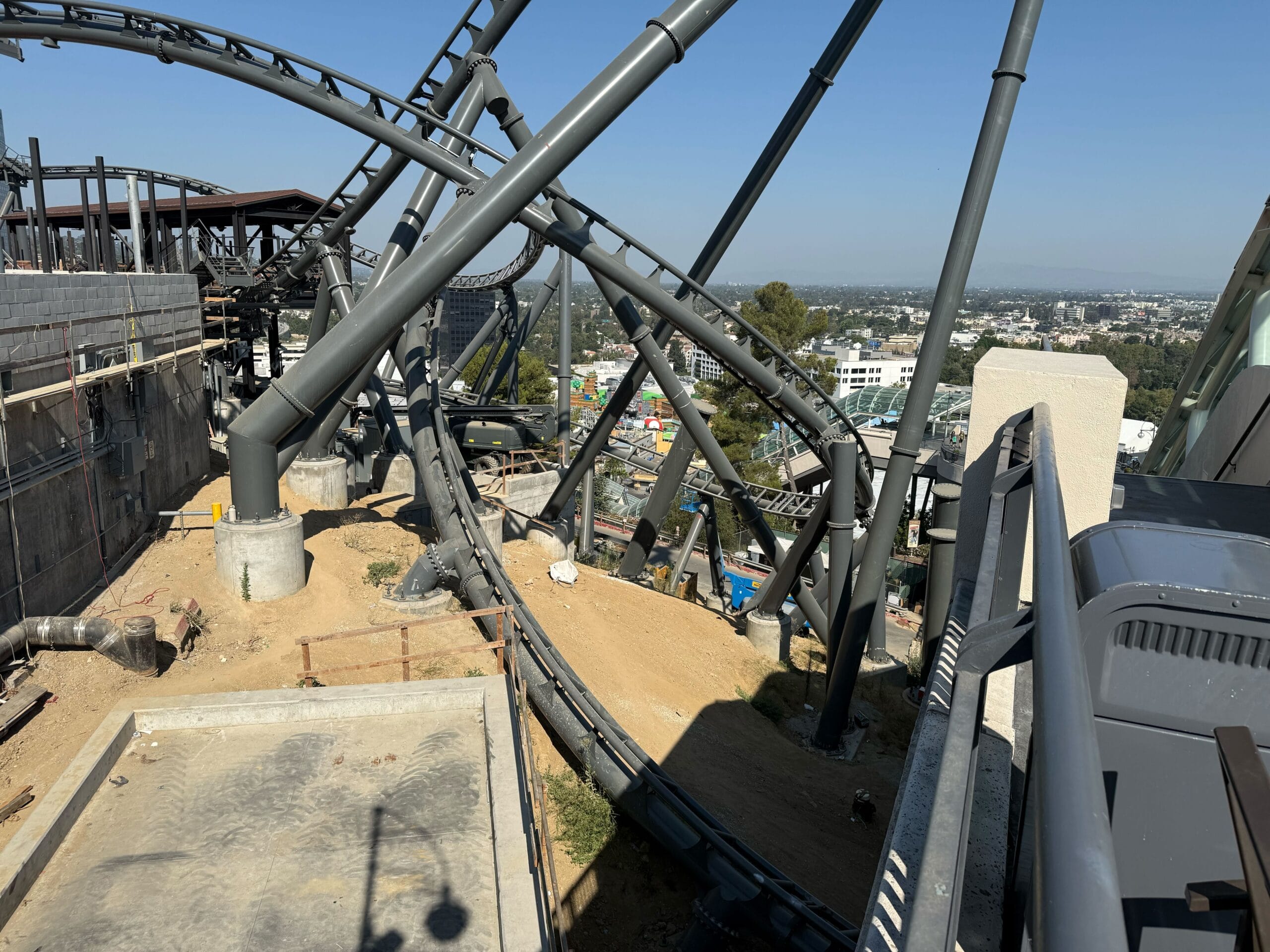 Roller coaster tracks twist and turn on a construction site at Universal Studios Hollywood, overlooking the cityscape.