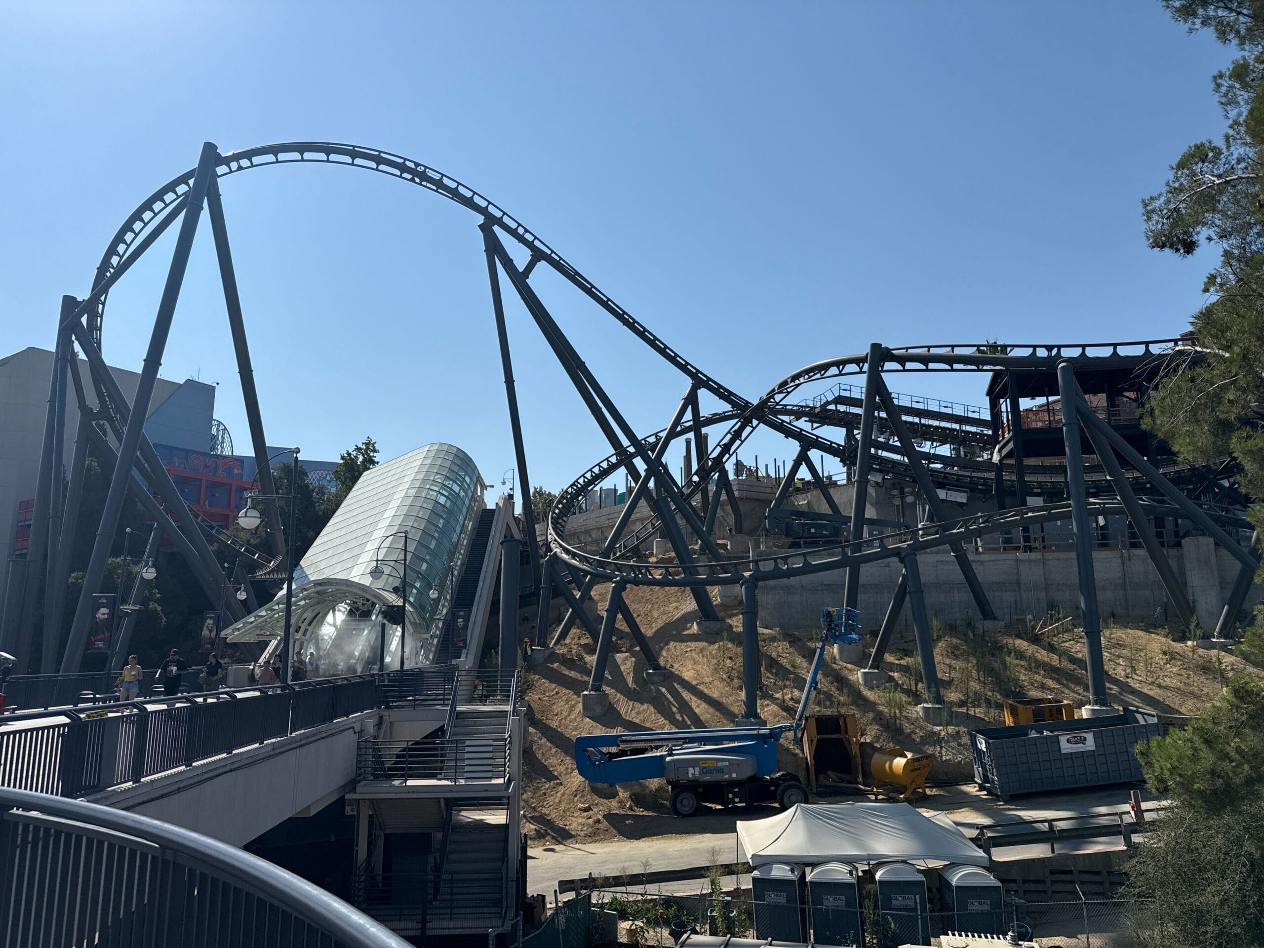 A large looping steel roller coaster twists under a clear blue sky in Universal Studios Hollywood, construction vehicles below.