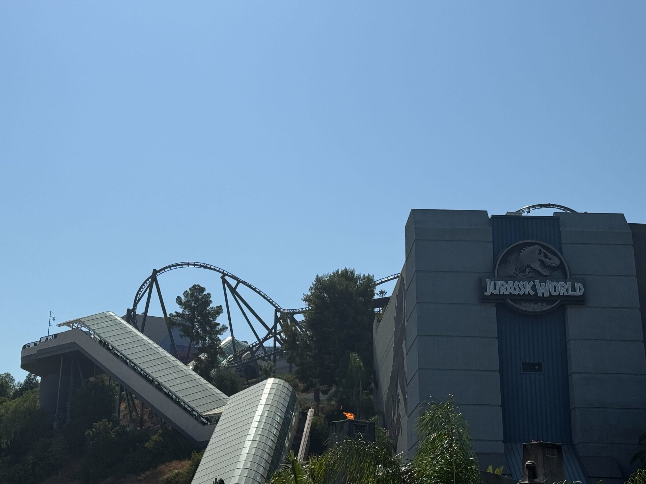 Jurassic World building and coaster at Universal Studios Hollywood, set against a clear blue sky with lush greenery.