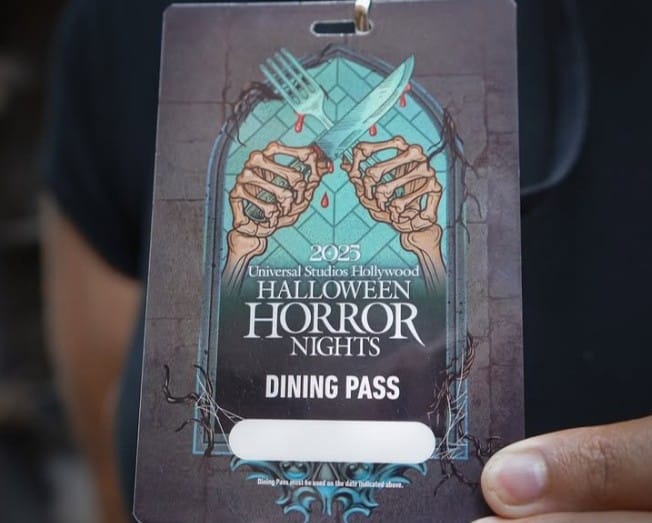A hand holds a Universal Studios Hollywood Dining Pass for 2023 Halloween Horror Nights, featuring a creepy knife and fork.