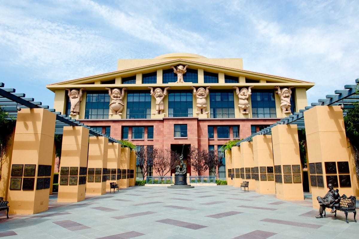 A Walt Disney Company building with large character statues holding up the roof and a central plaza lined with pillars and plaques.