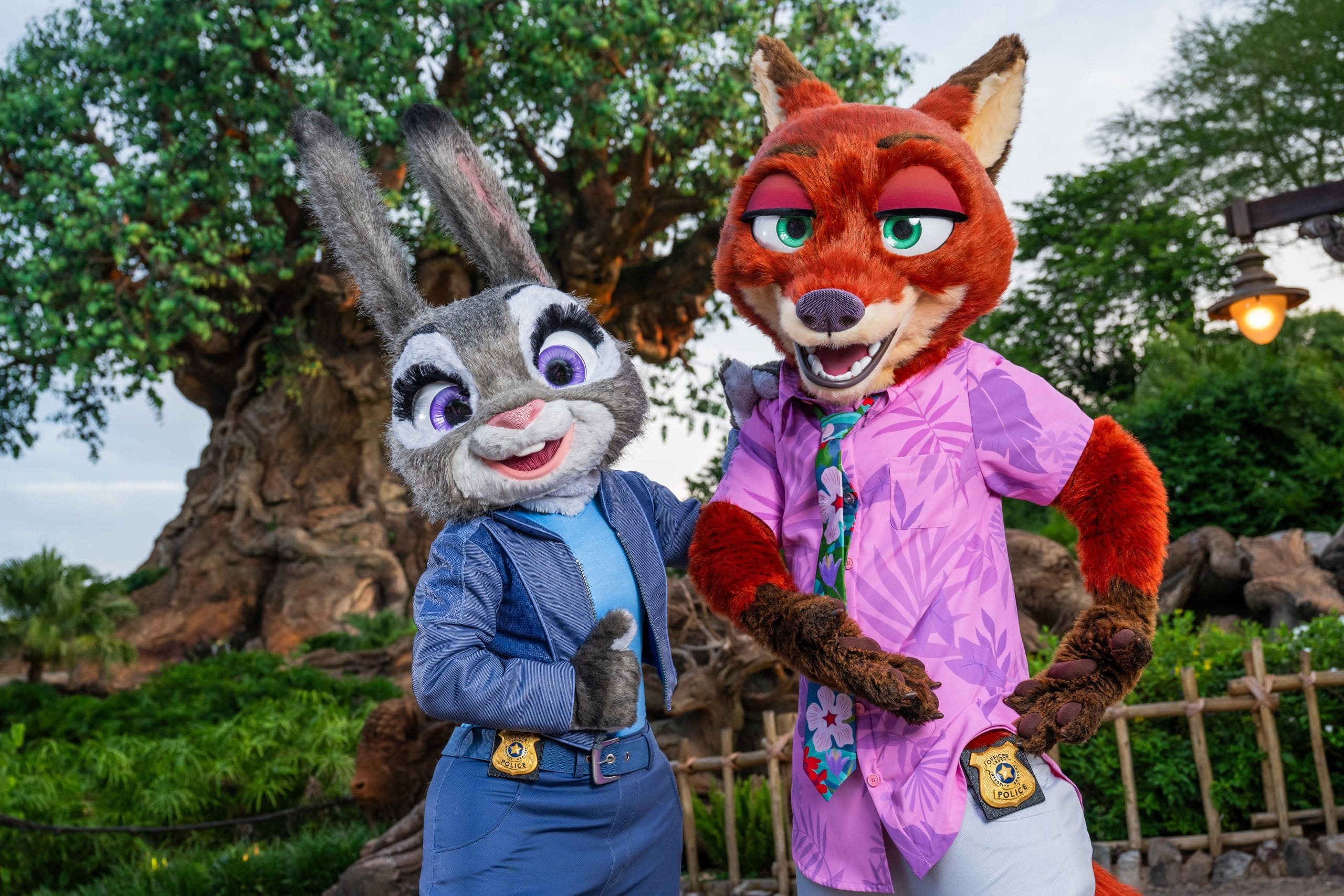 Two people in Judy Hopps and Nick Wilde costumes pose by a large tree, showcasing Zootopia details at a theme park.