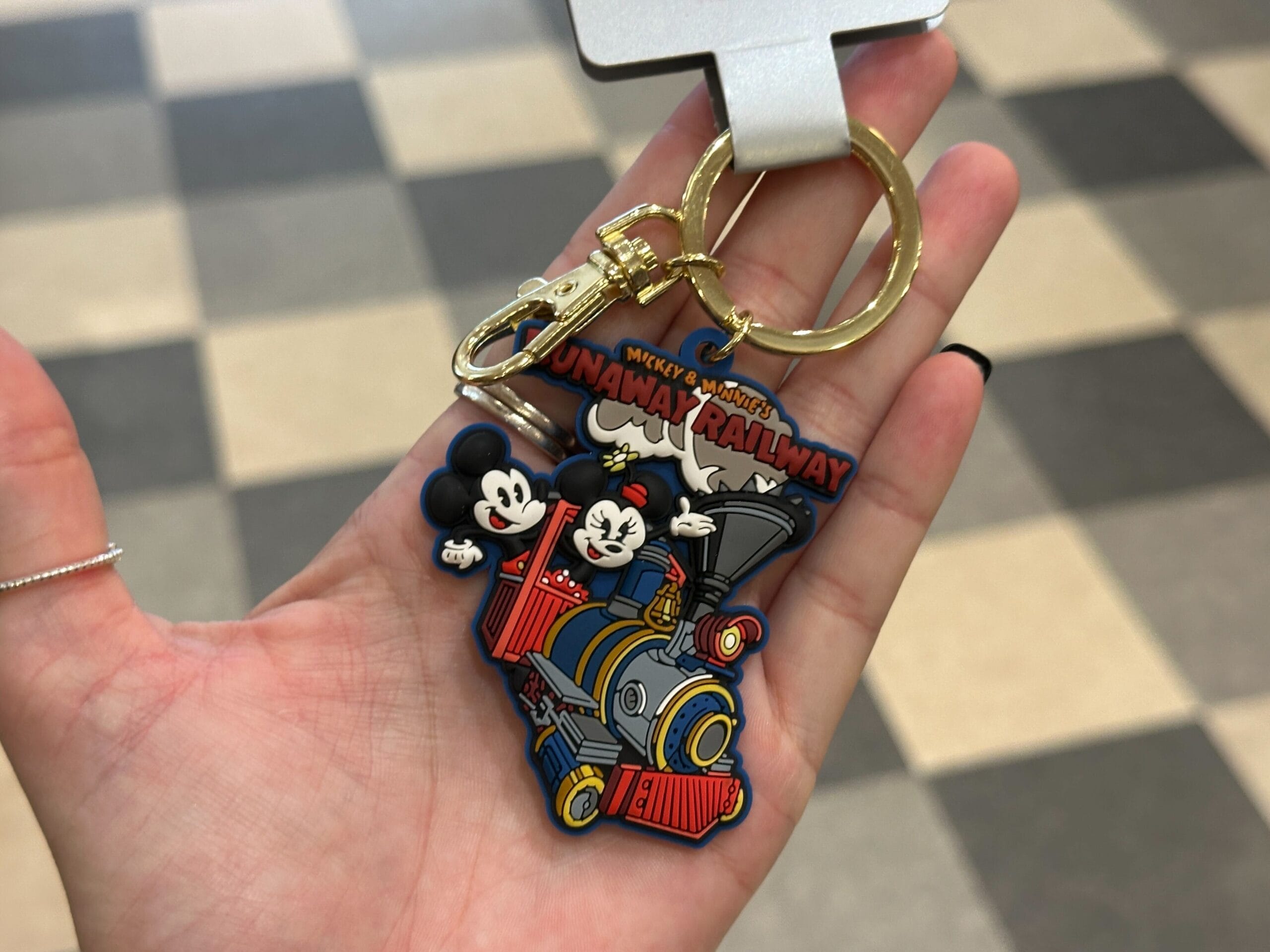 A hand holds a keychain featuring Mickey and Minnie Mouse on a train labeled "Runaway Railway.