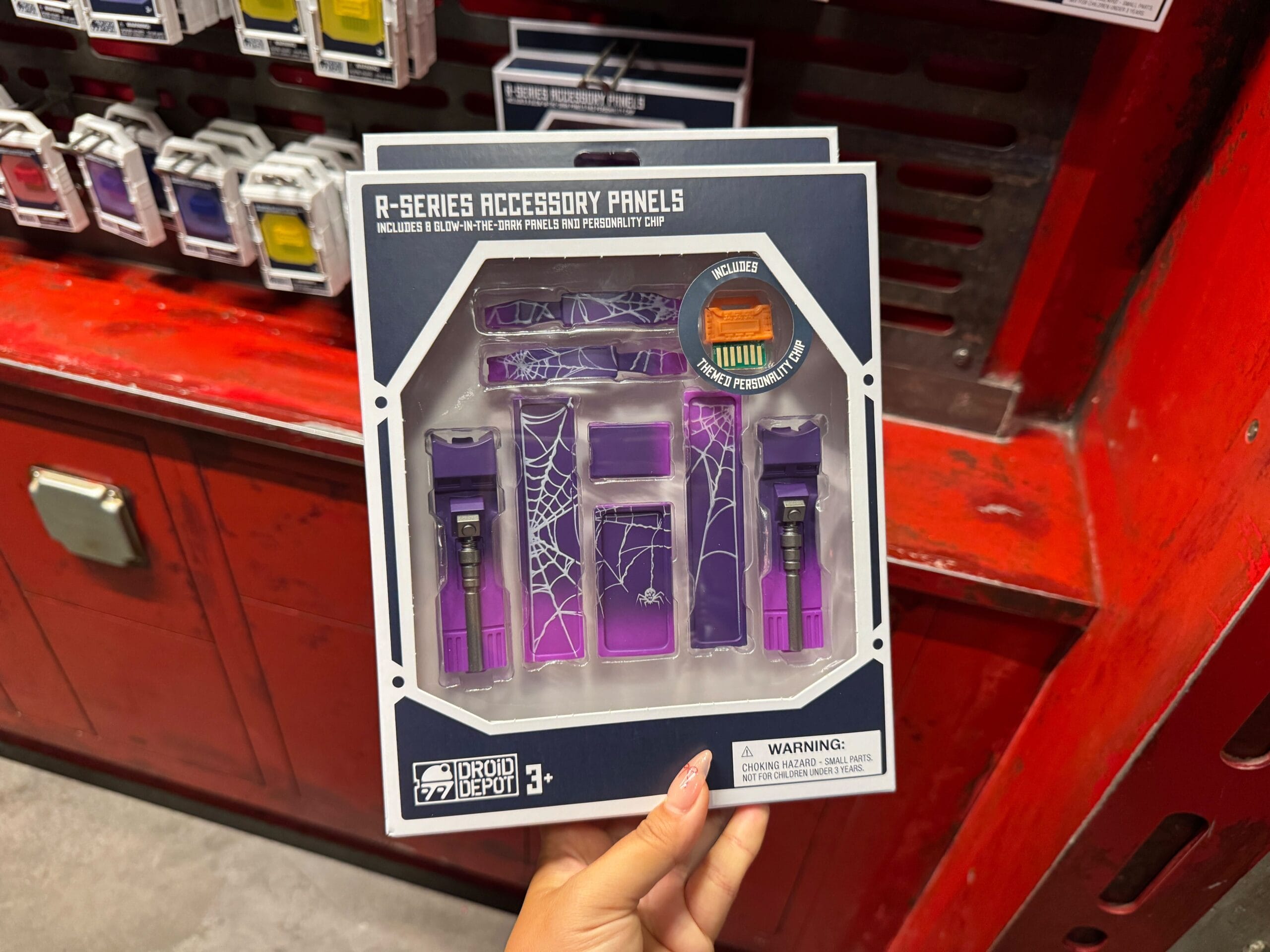 Hand holding R-Series Droid Depot accessory panels in purple with spiderweb design, displayed in packaging.