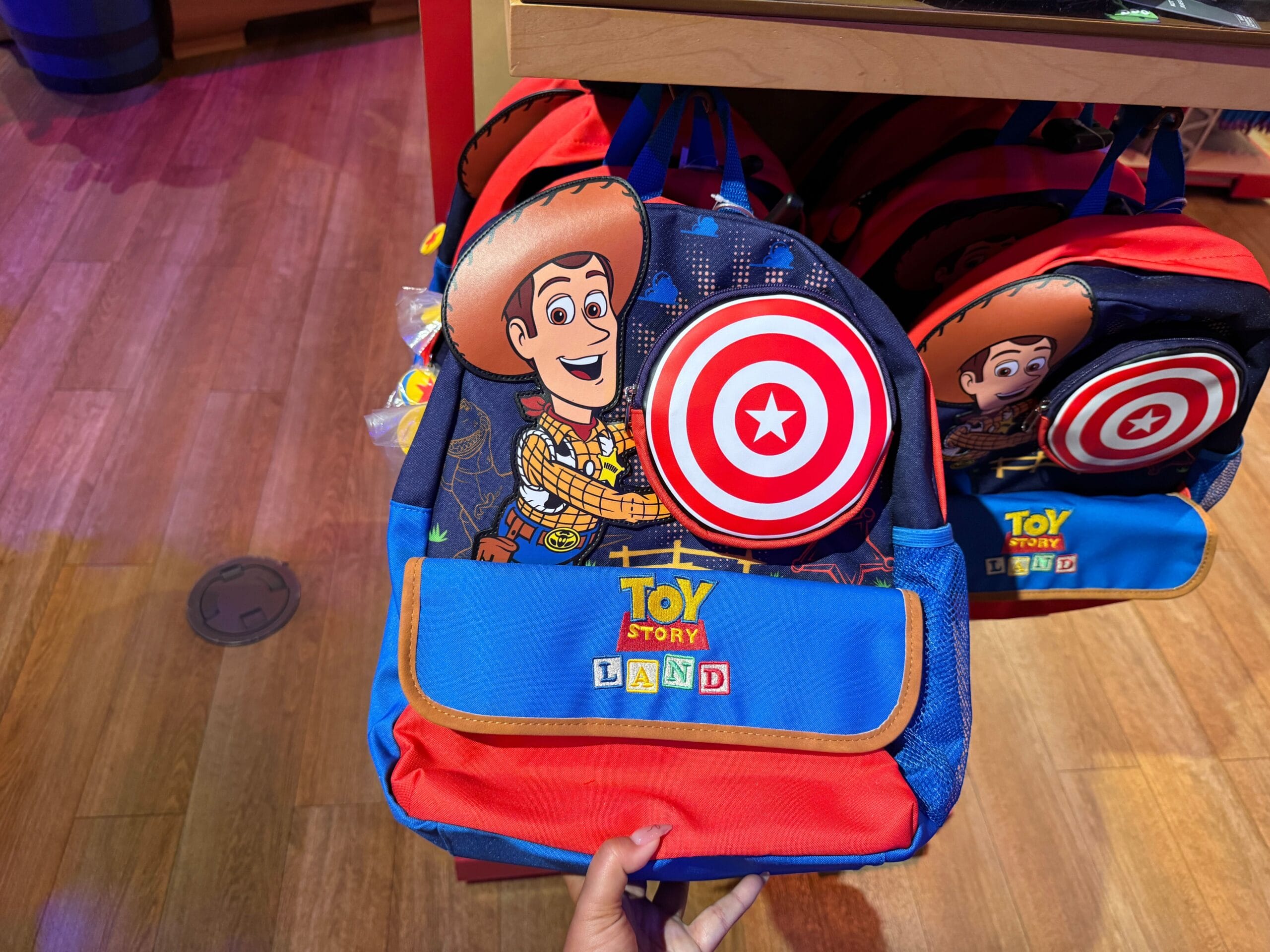 A colorful Toy Story Land backpack featuring Woody and a red target design on display in a store.