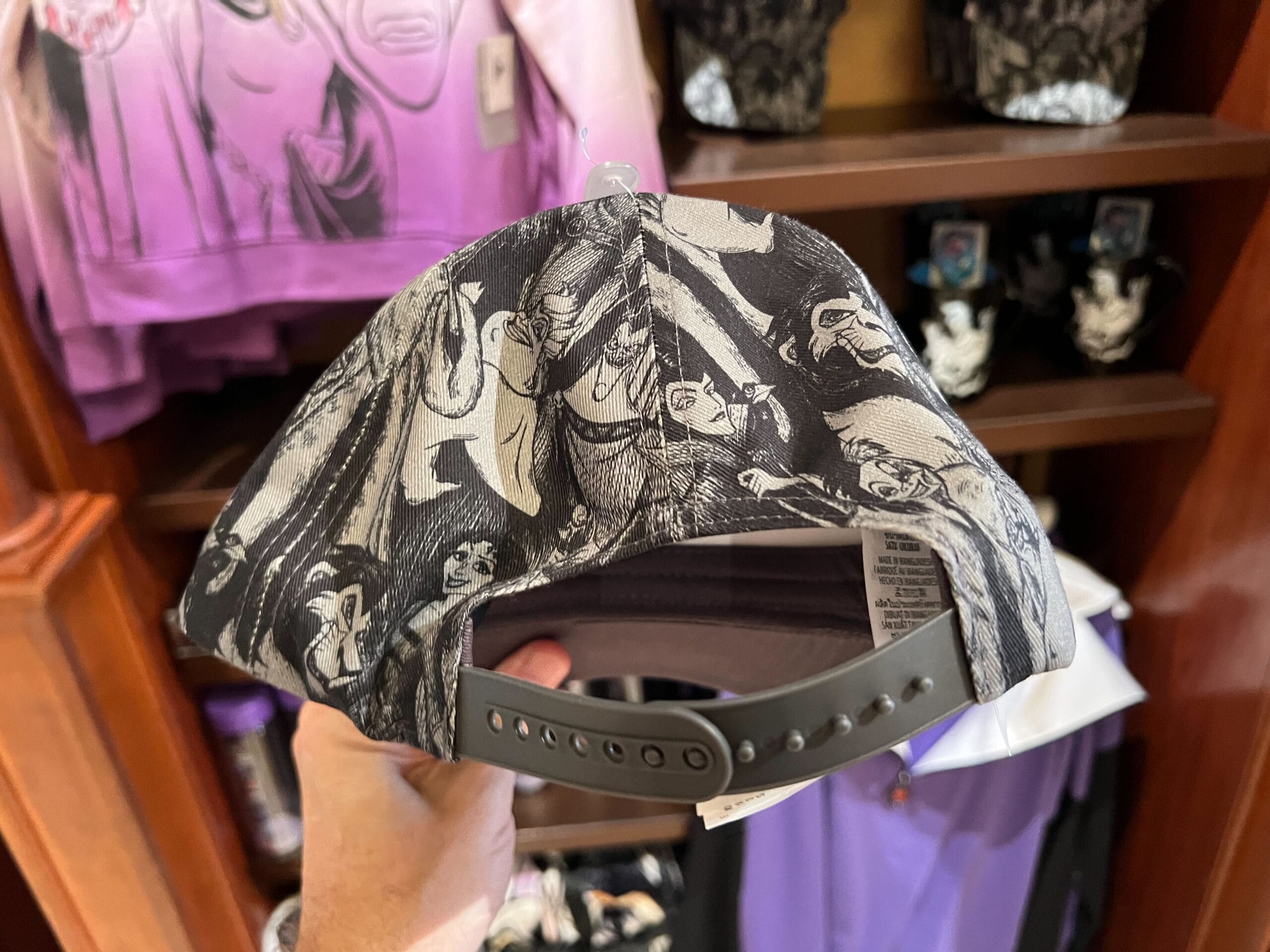 A hand holds a black-and-white Walt Disney World hat featuring Disney Villains merchandise, displayed in a store.