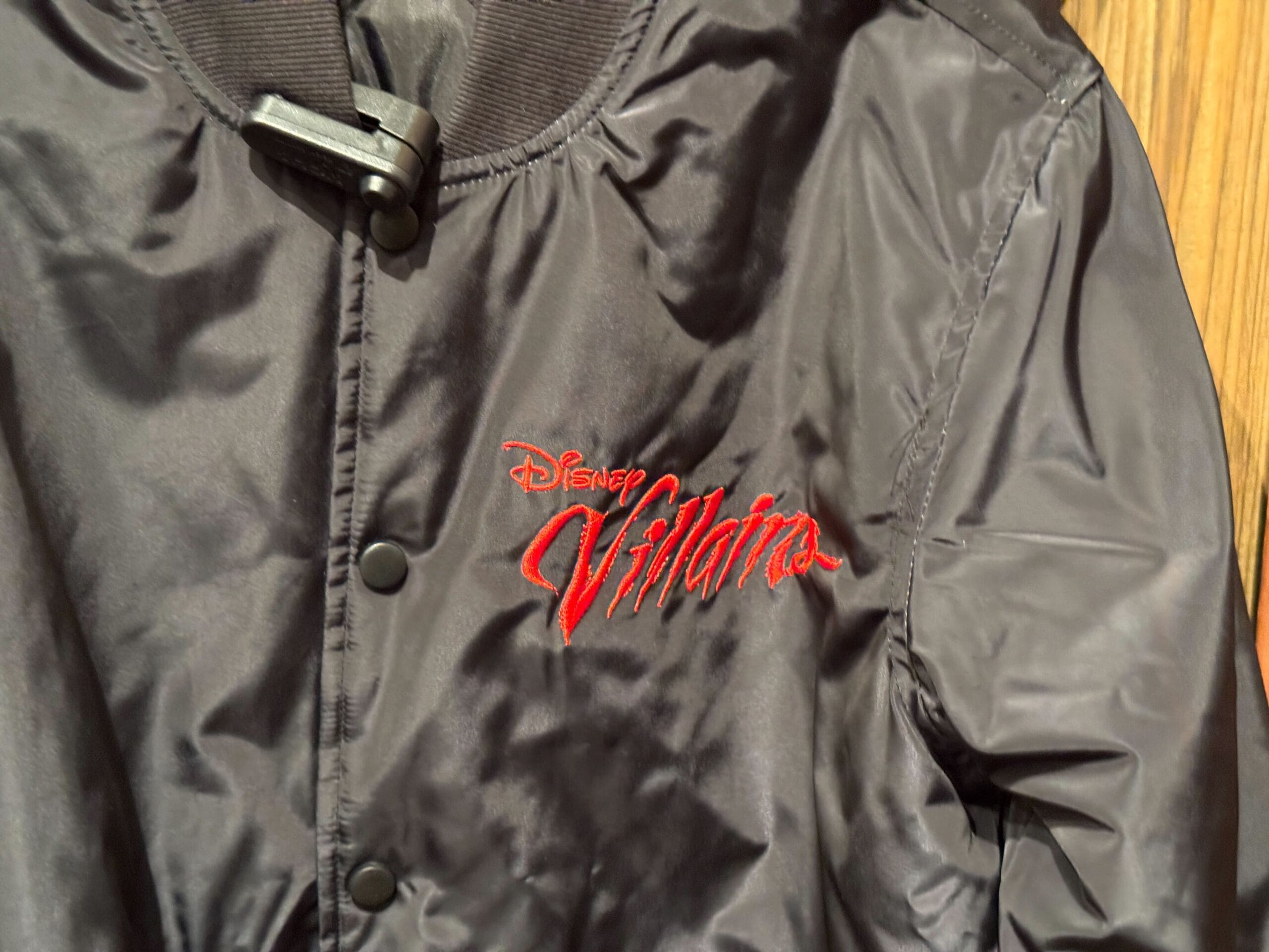 Black satin jacket with "Disney Villains" embroidered in red script on the chest.