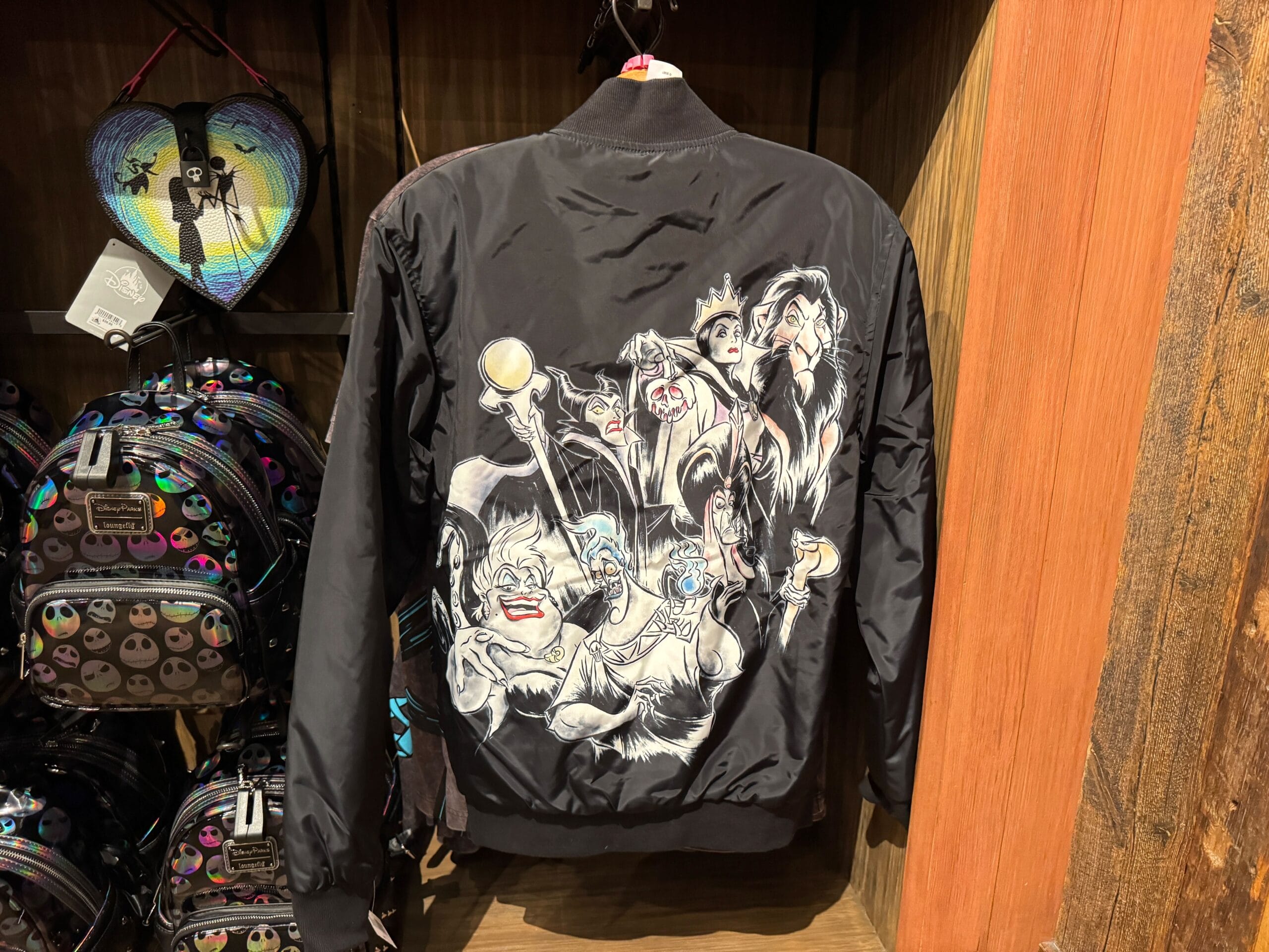 Black jacket featuring Disney villains artwork hanging on a rack, surrounded by themed bags and wallets.