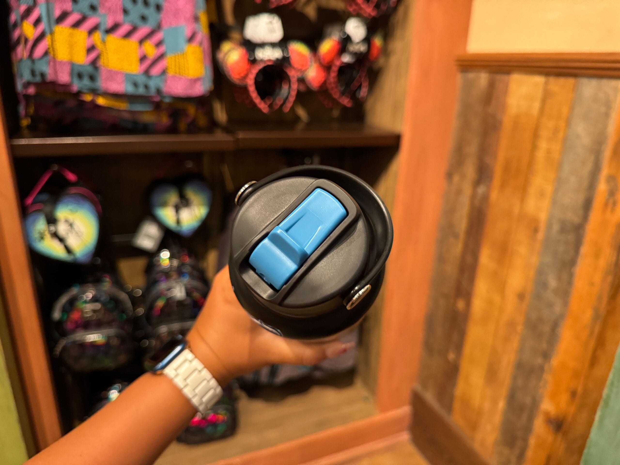 A hand holds a black water bottle with a blue flip-top lid in front of Disney Villains merchandise.