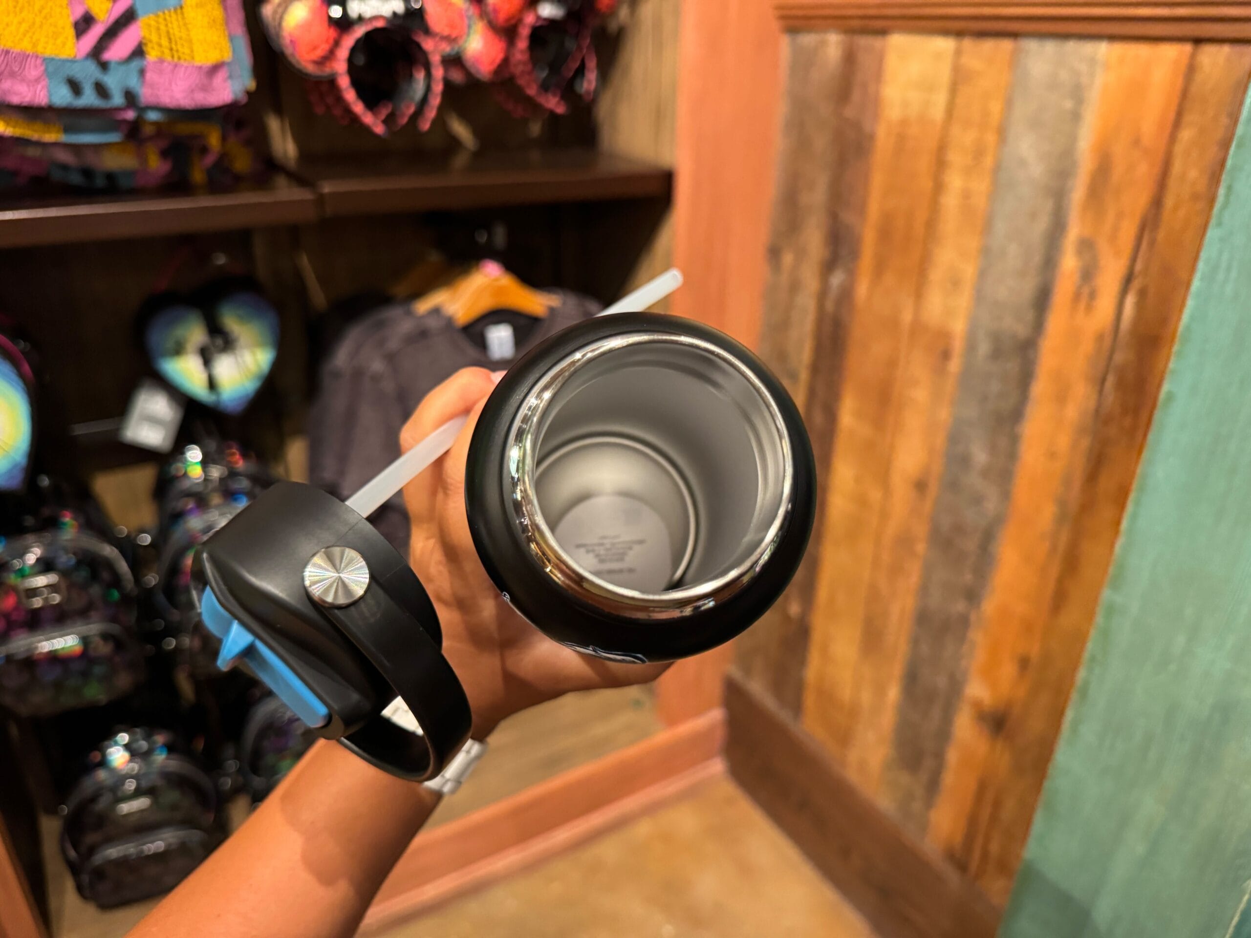 A person holds an open black water bottle with a straw in a store selling Disney Villains merchandise.