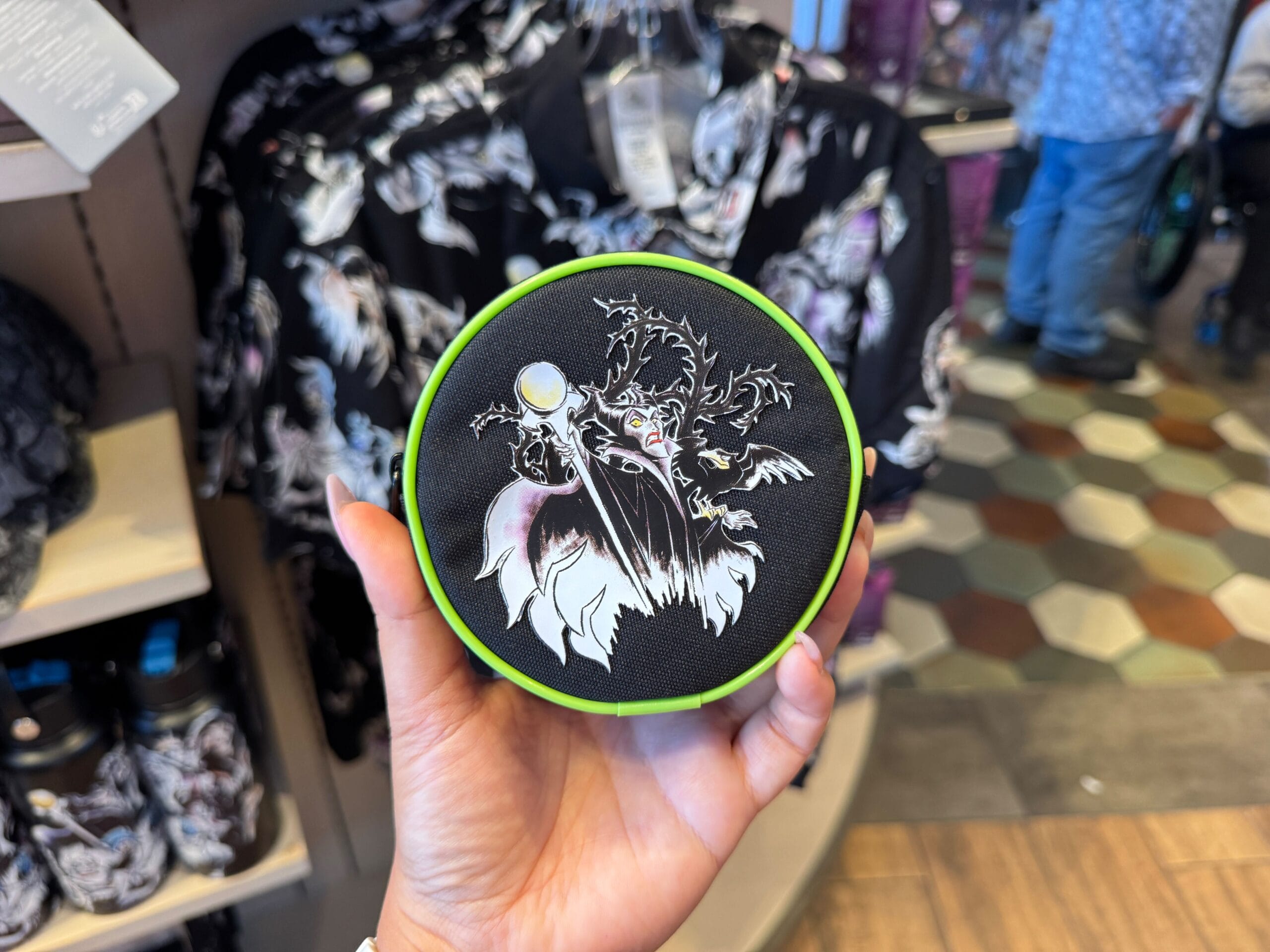 A hand displays a Maleficent patch in front of matching shirts—perfect Disney Villains merchandise for Halloween 2025.