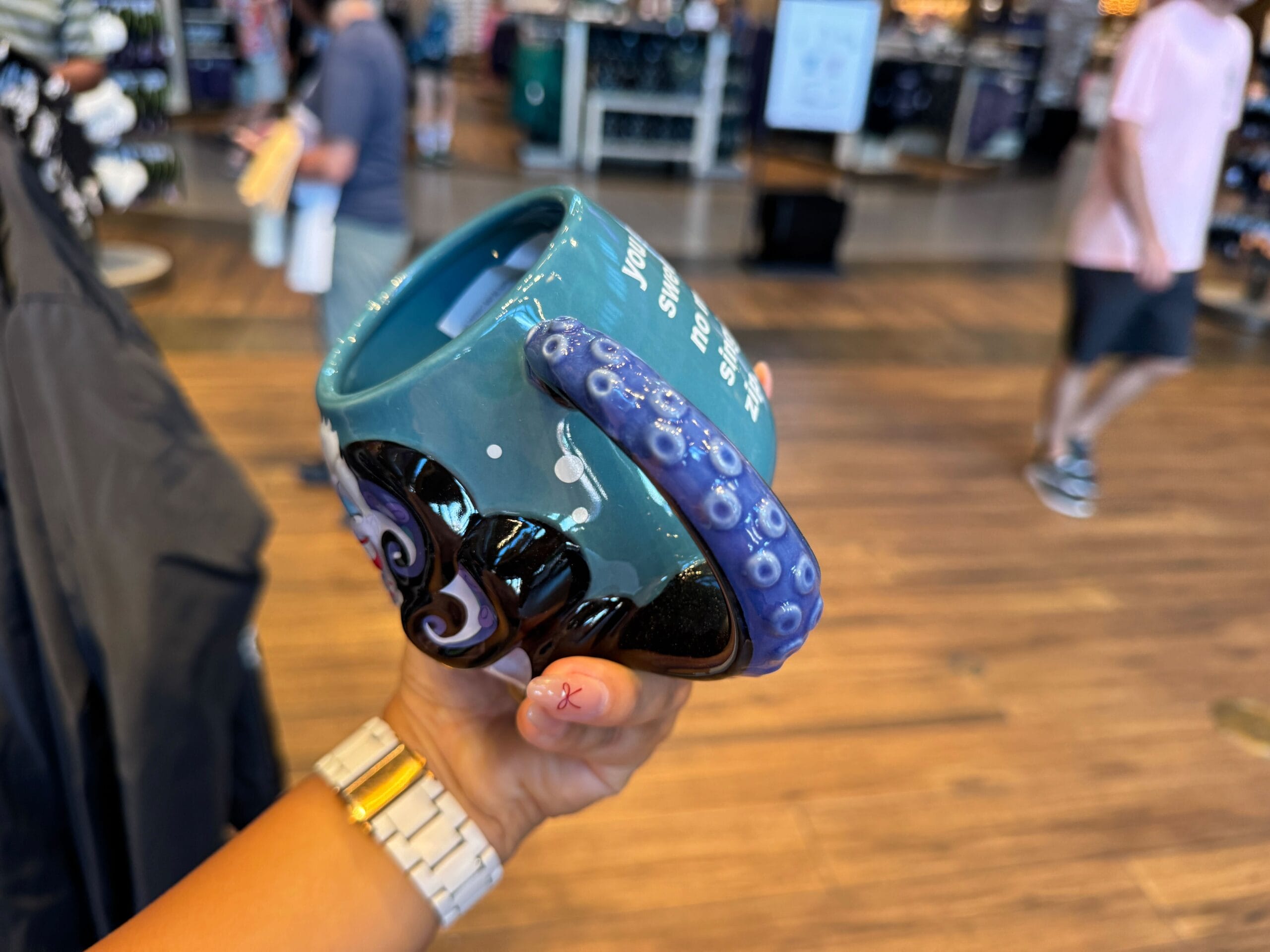A hand holds a blue mug with a purple octopus tentacle handle, perfect for Disney Villains merchandise lovers.