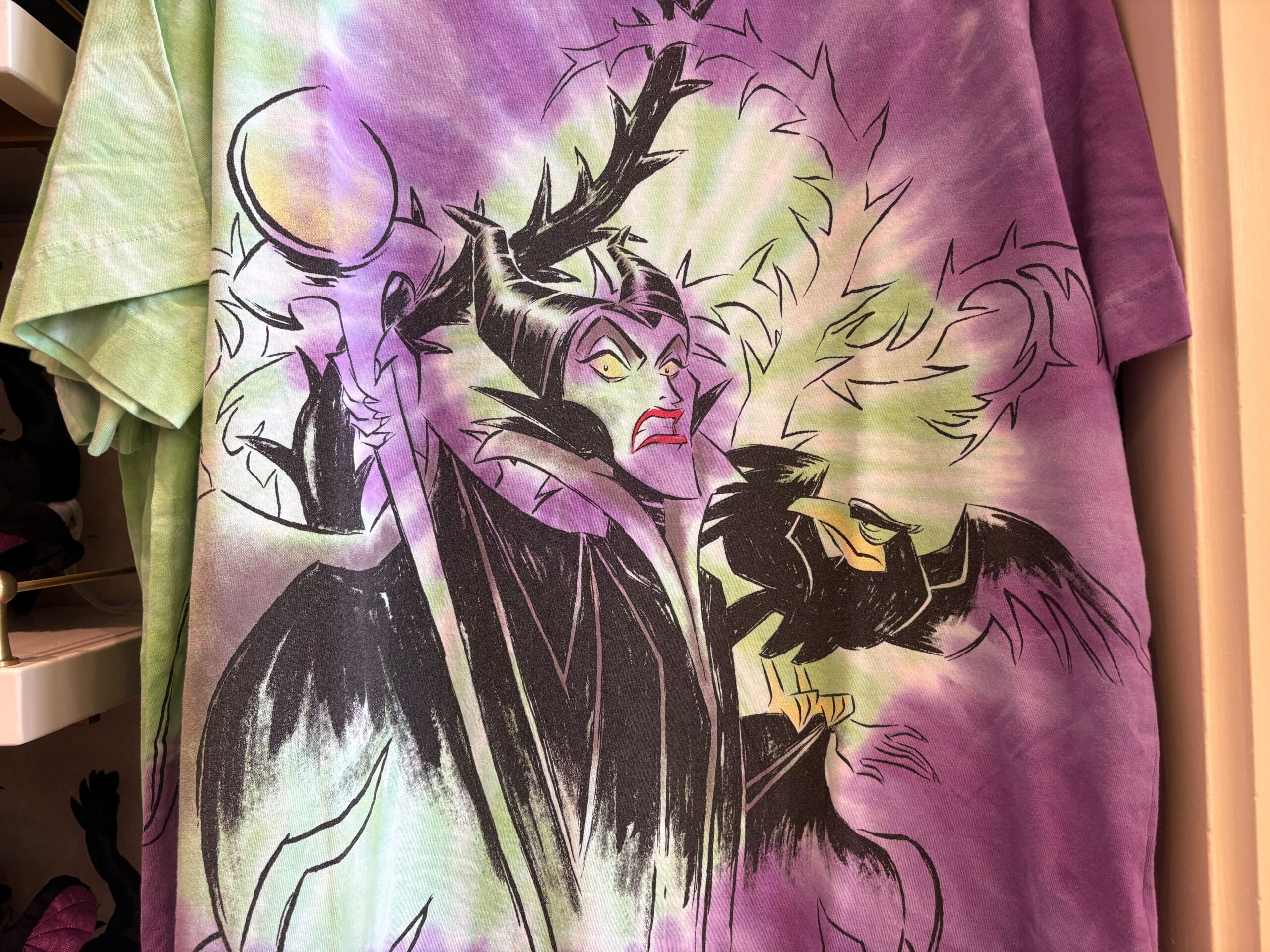 Tie-dye shirt featuring Maleficent and her raven amid green and purple flames—perfect Disney Villains merchandise for Halloween 2025.