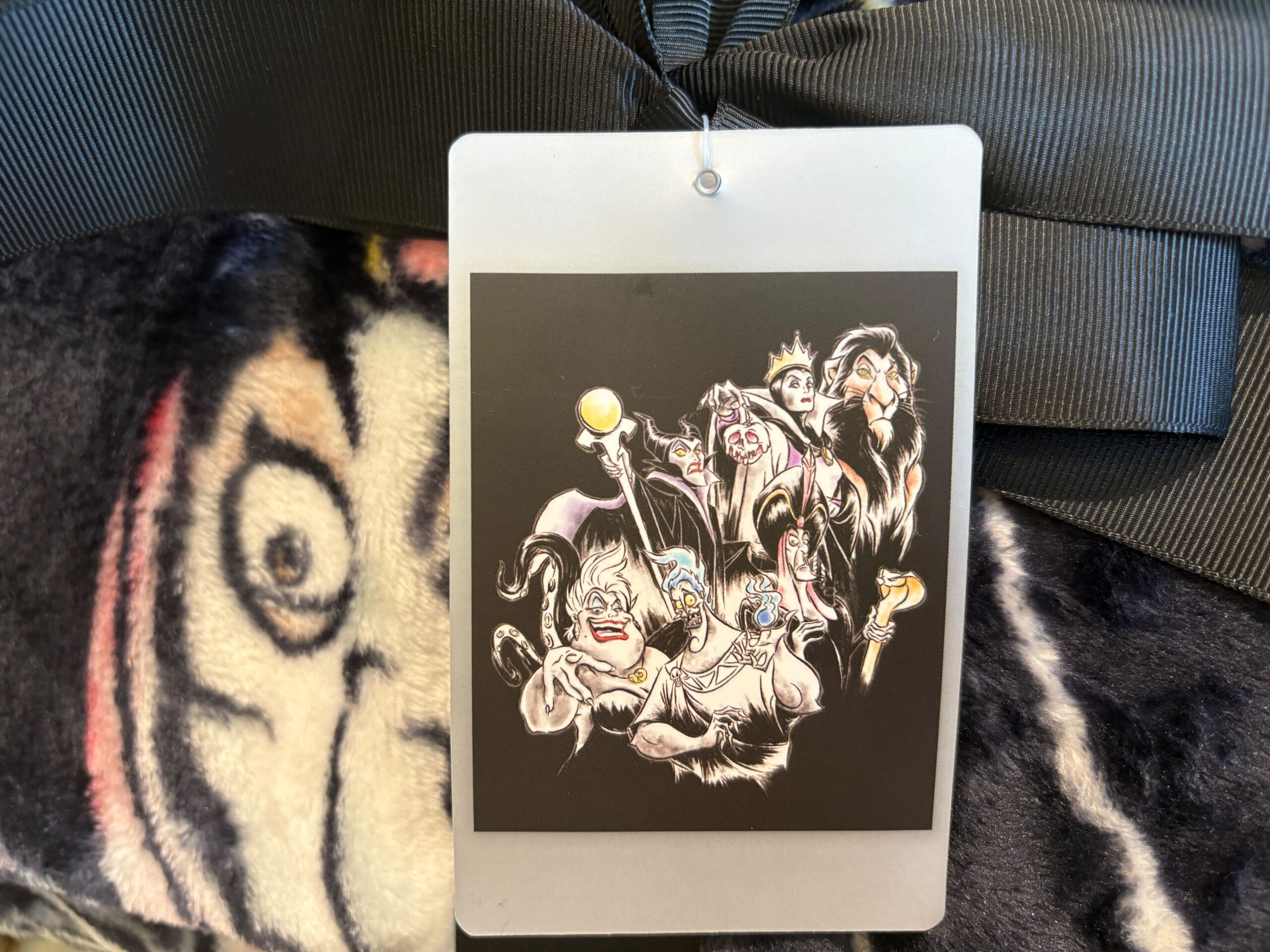 A badge with illustrated Disney Villains merchandise hangs on a black ribbon against a fuzzy, patterned background.