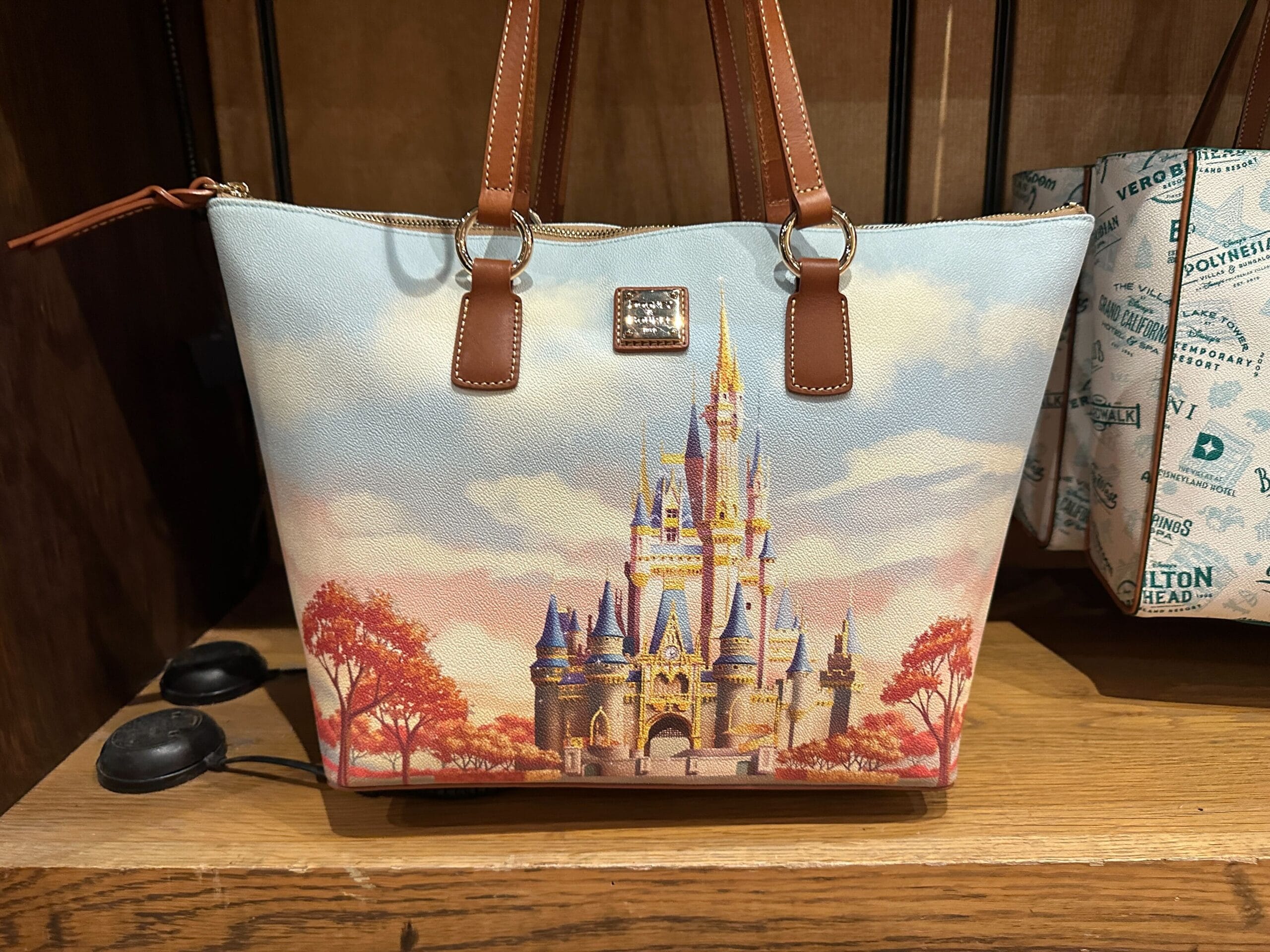 A handbag with an illustration of a fairytale castle, autumn trees, and blue sky, displayed on a wooden shelf.