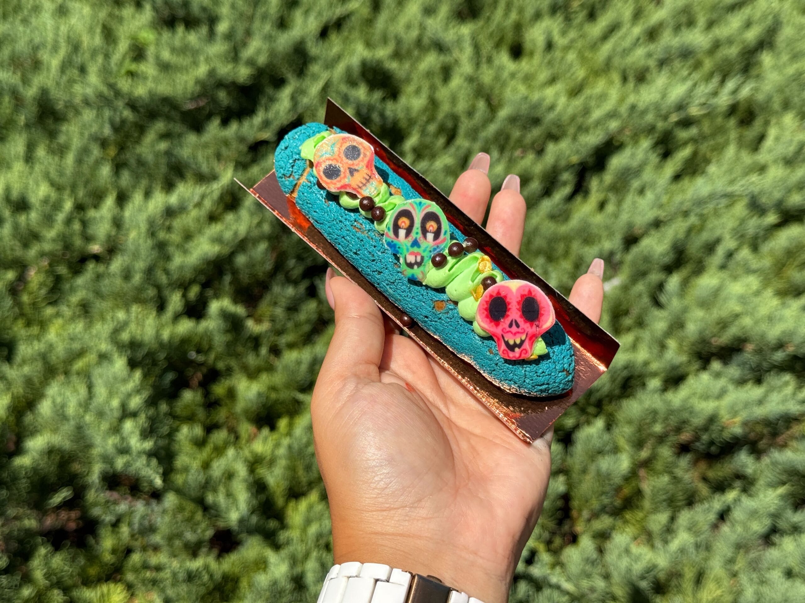 A hand holds a blue éclair with skulls and green frosting—perfect Halloween food to try at Disney Springs.