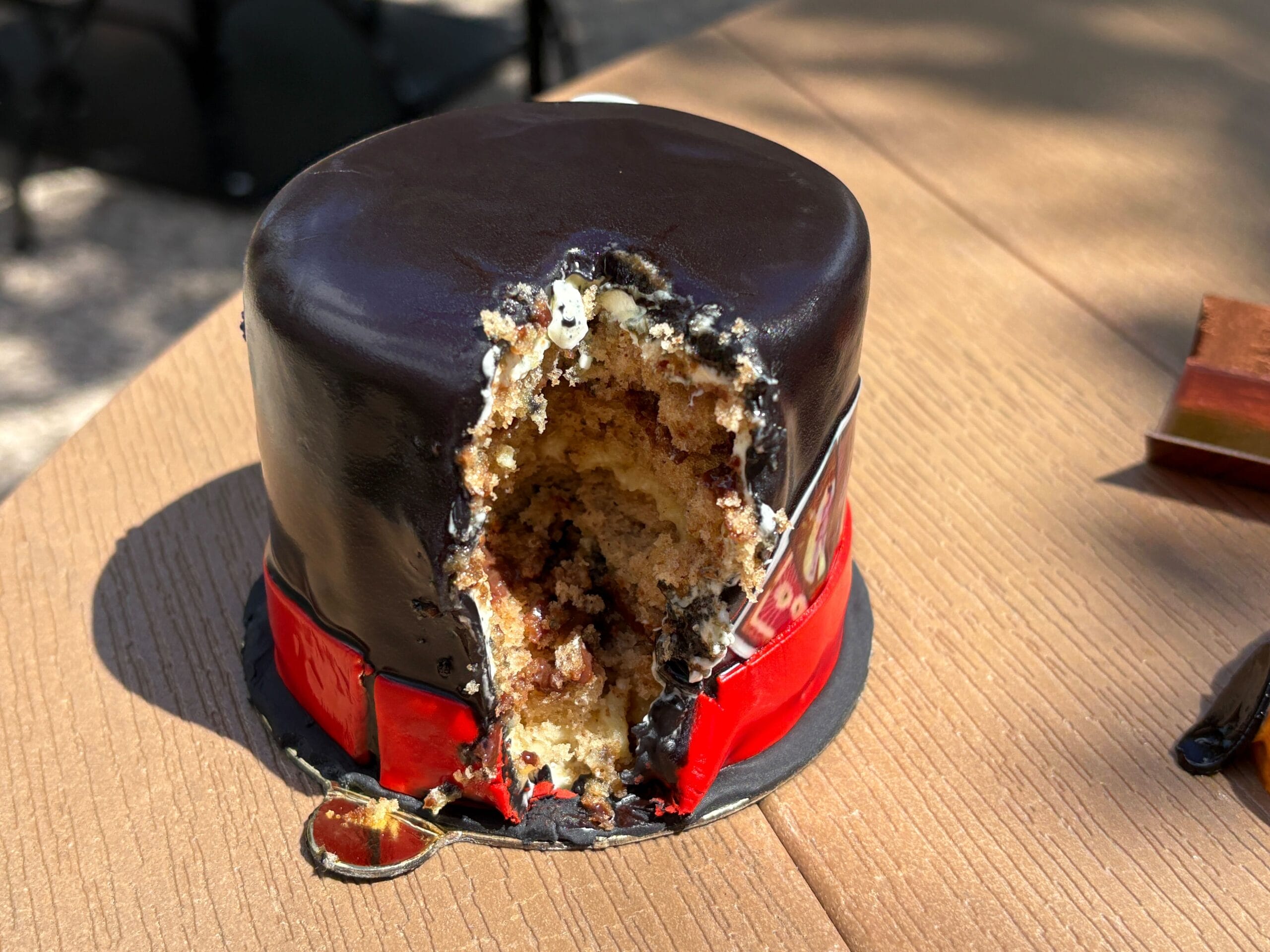 A small chocolate-covered cake, perfect for Halloween food reviews, sits on a wooden table in sunlight.
