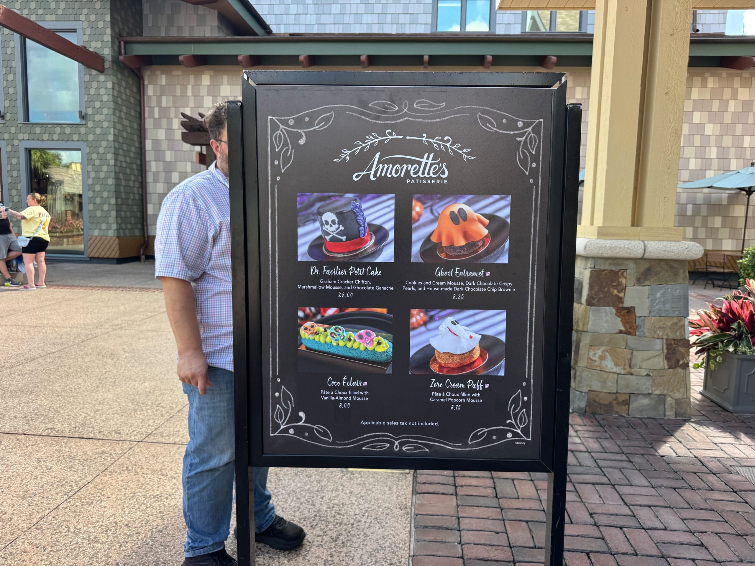 A menu board at Disney Springs’ Amorette’s Patisserie shows photos and names of four Halloween Food desserts outside the shop.