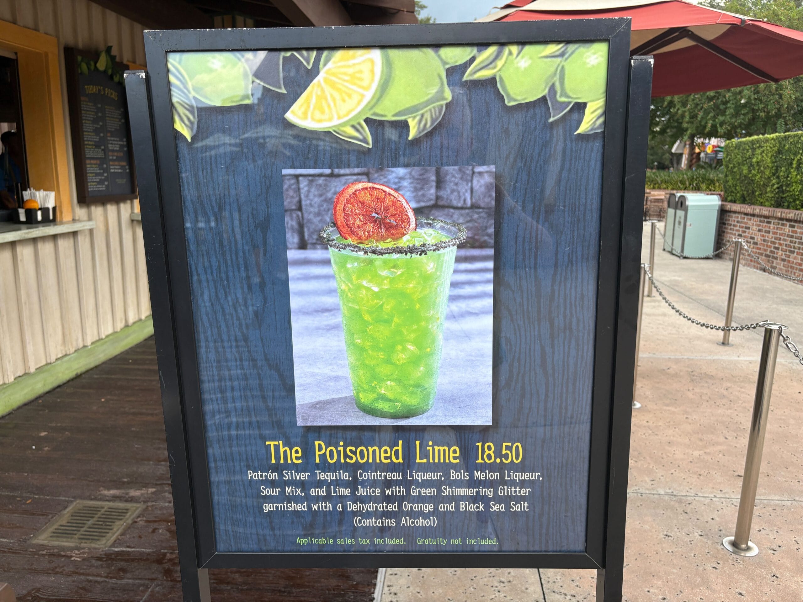 A sign at Disney Springs displays a bright green cocktail called "The Poisoned Lime" with a dried lime garnish and details.