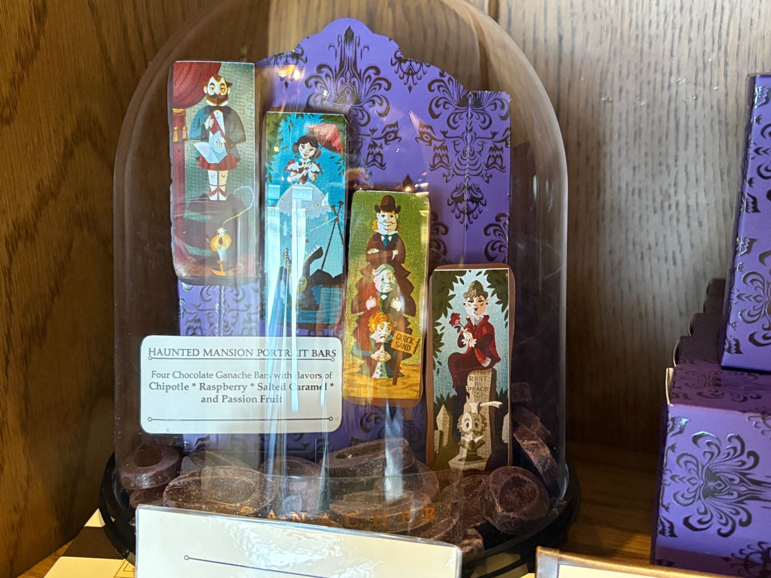 Four illustrated chocolate bars with Haunted Mansion characters under a clear display dome at Disney Springs.