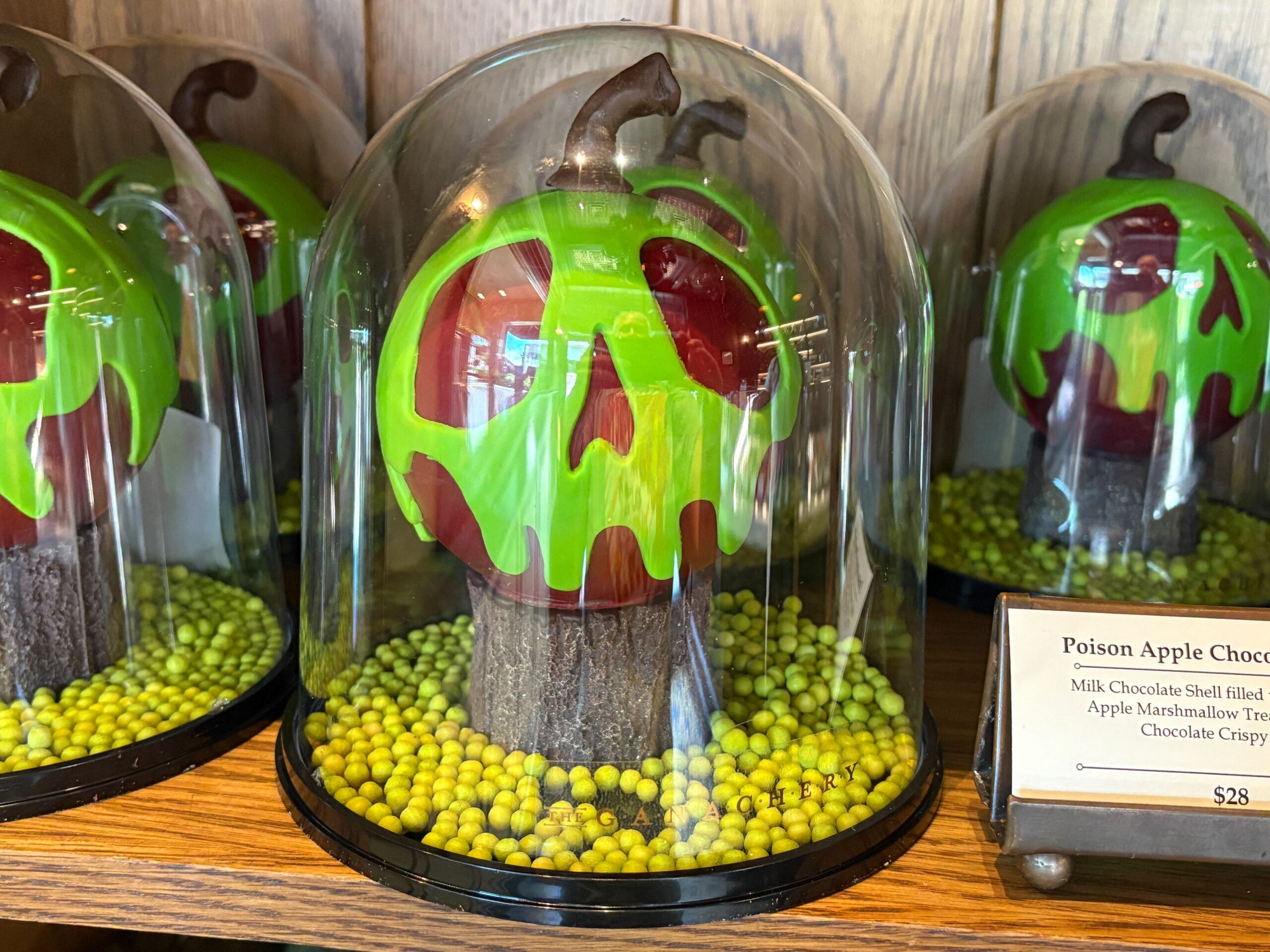 Large chocolate apples with green skulls, a spooky Halloween food at Disney Springs, displayed under glass domes.
