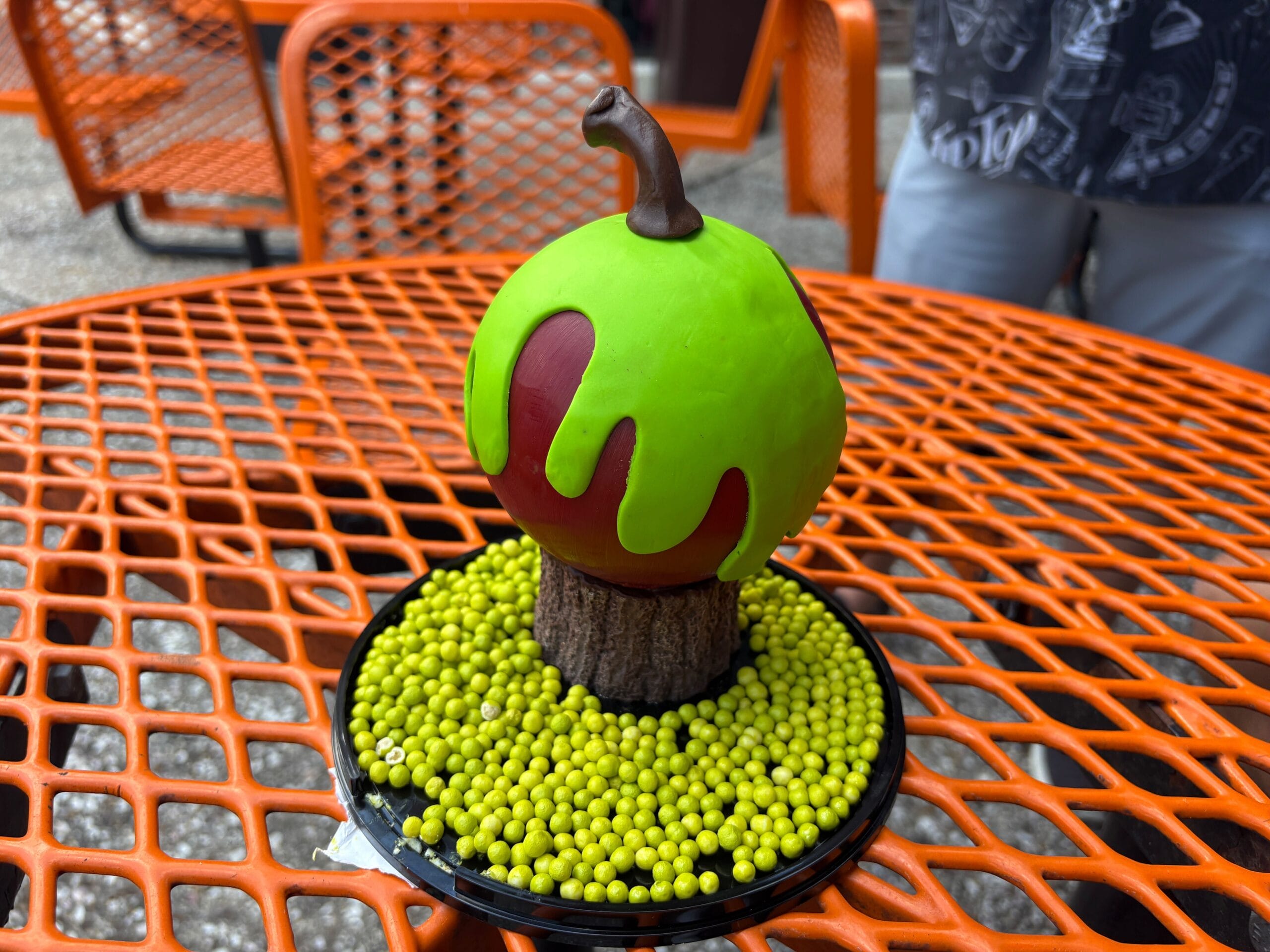 A dessert shaped like an apple with green glaze sits on yellow candy balls at Disney Springs.