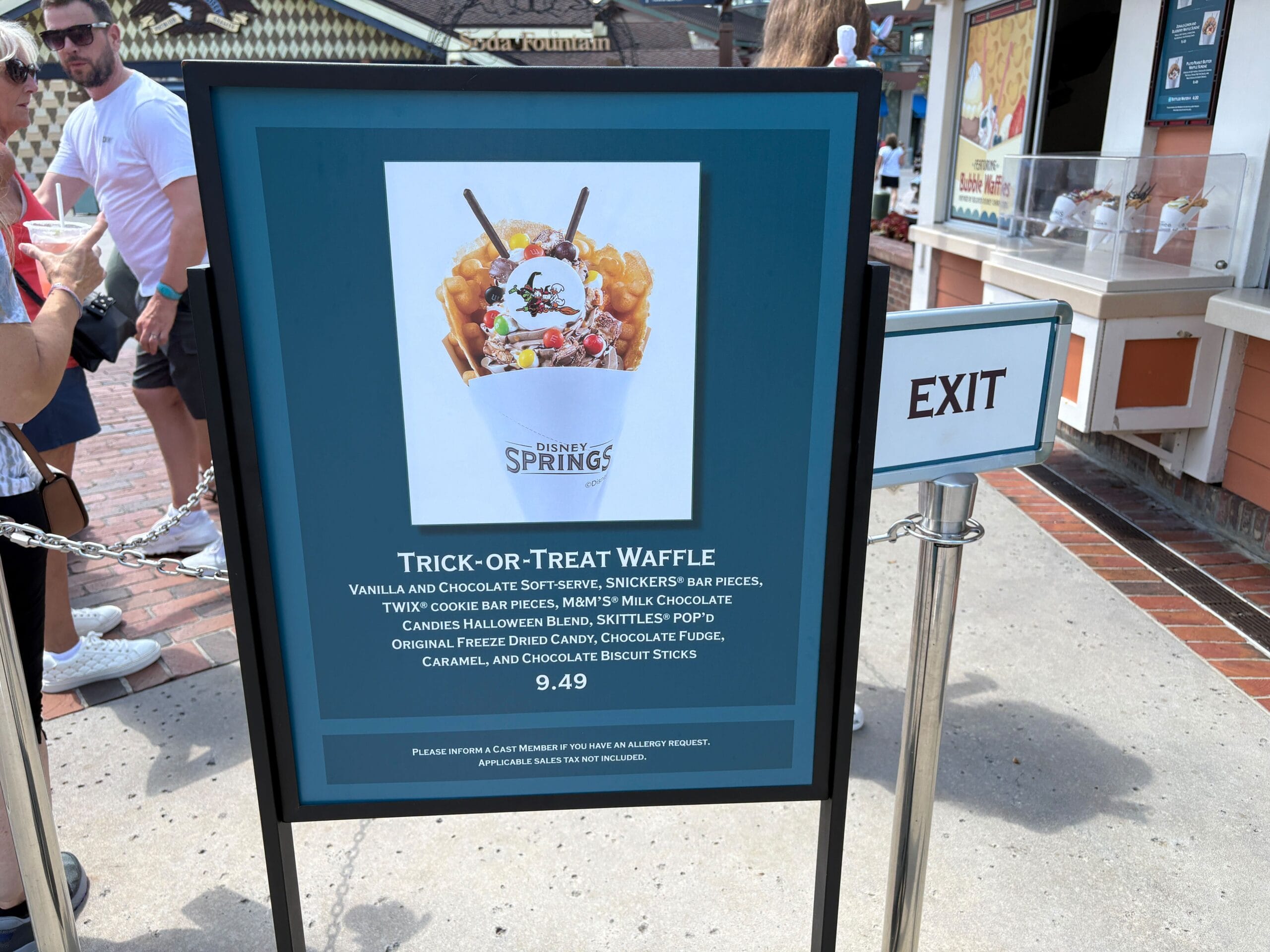 Sign displays "Trick-or-Treat Waffle" with description and price, near the EXIT at Disney Springs for Halloween.