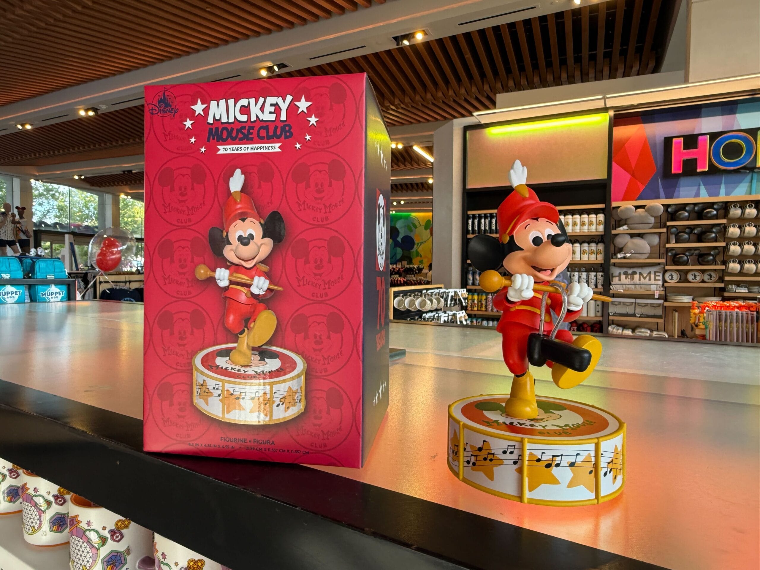 Mickey Mouse Club figurine in a band uniform stands by its red box in a brightly lit store.
