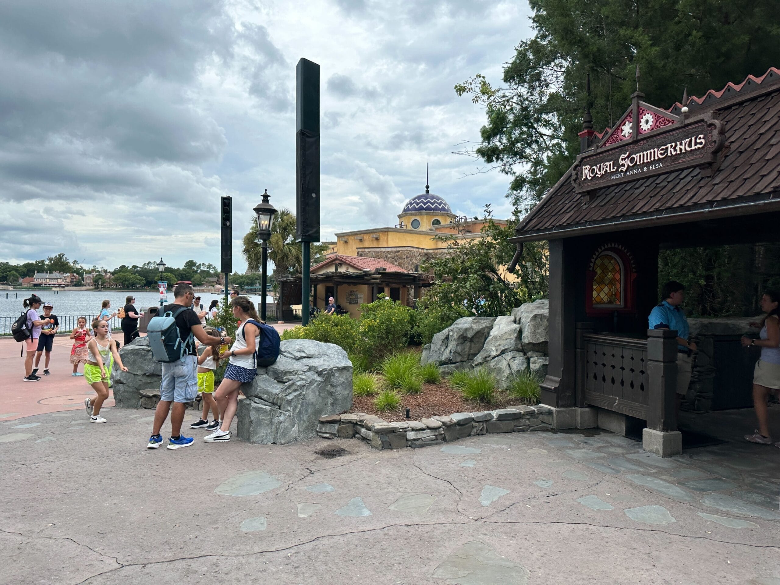 Visitors walk near the Royal Sommerhus under cloudy skies at a themed amusement park area with landscaping and buildings.
