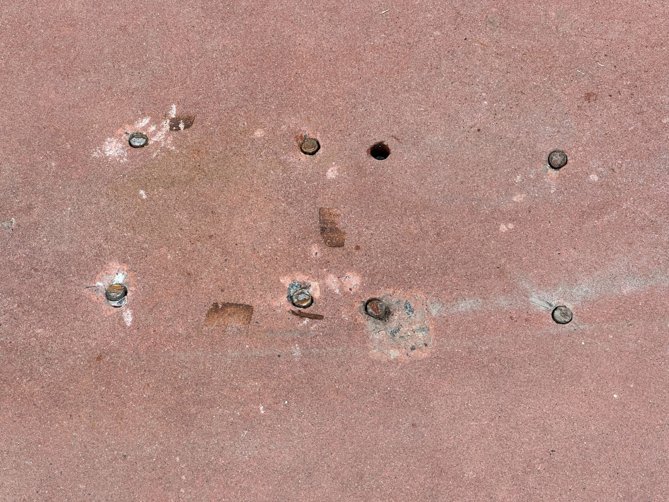 Rusty bolts and holes on a weathered, reddish metal surface, showing signs of wear and aging.