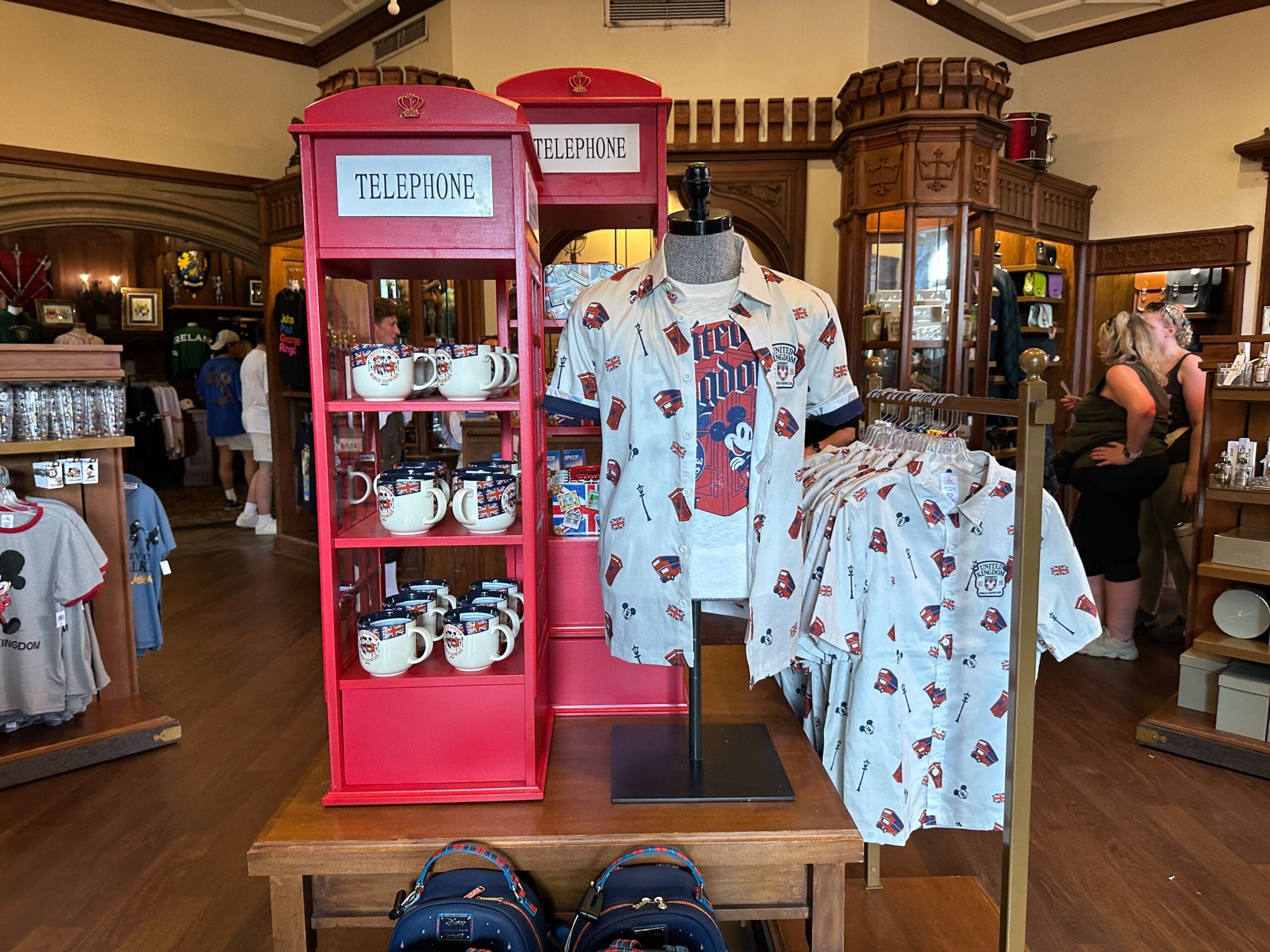 Display of UK-themed souvenir shirts and mugs next to red telephone booth shelves in a gift shop.